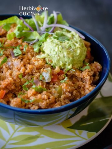 A blue bowl with Spanish quinoa, topped with guacamole and onions.