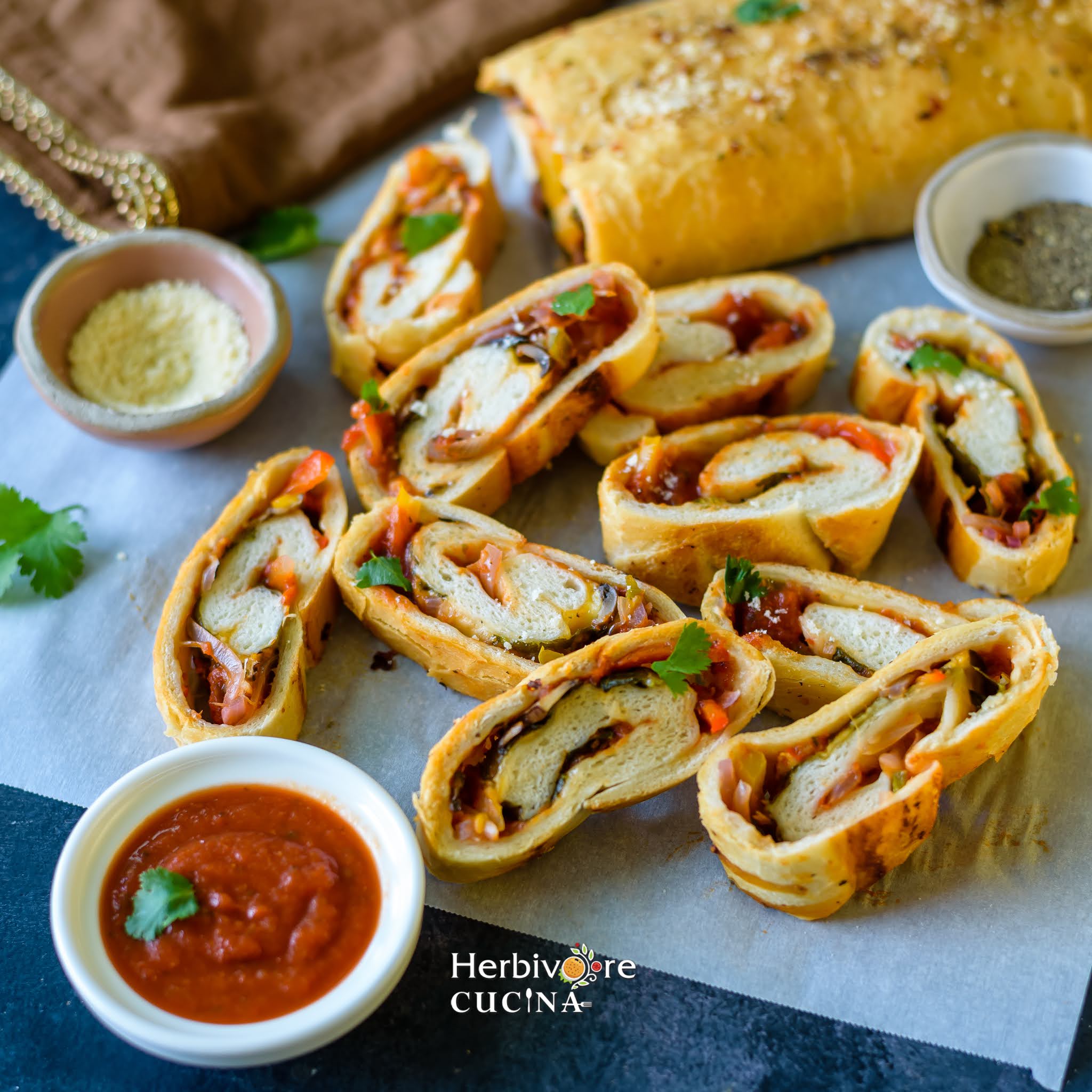 Slices of rolled up Stromboli on a white paper with cheese and sauce on the side. 