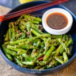 Stir Fried Asparagus in a blue bowl with chili oil placed by it.