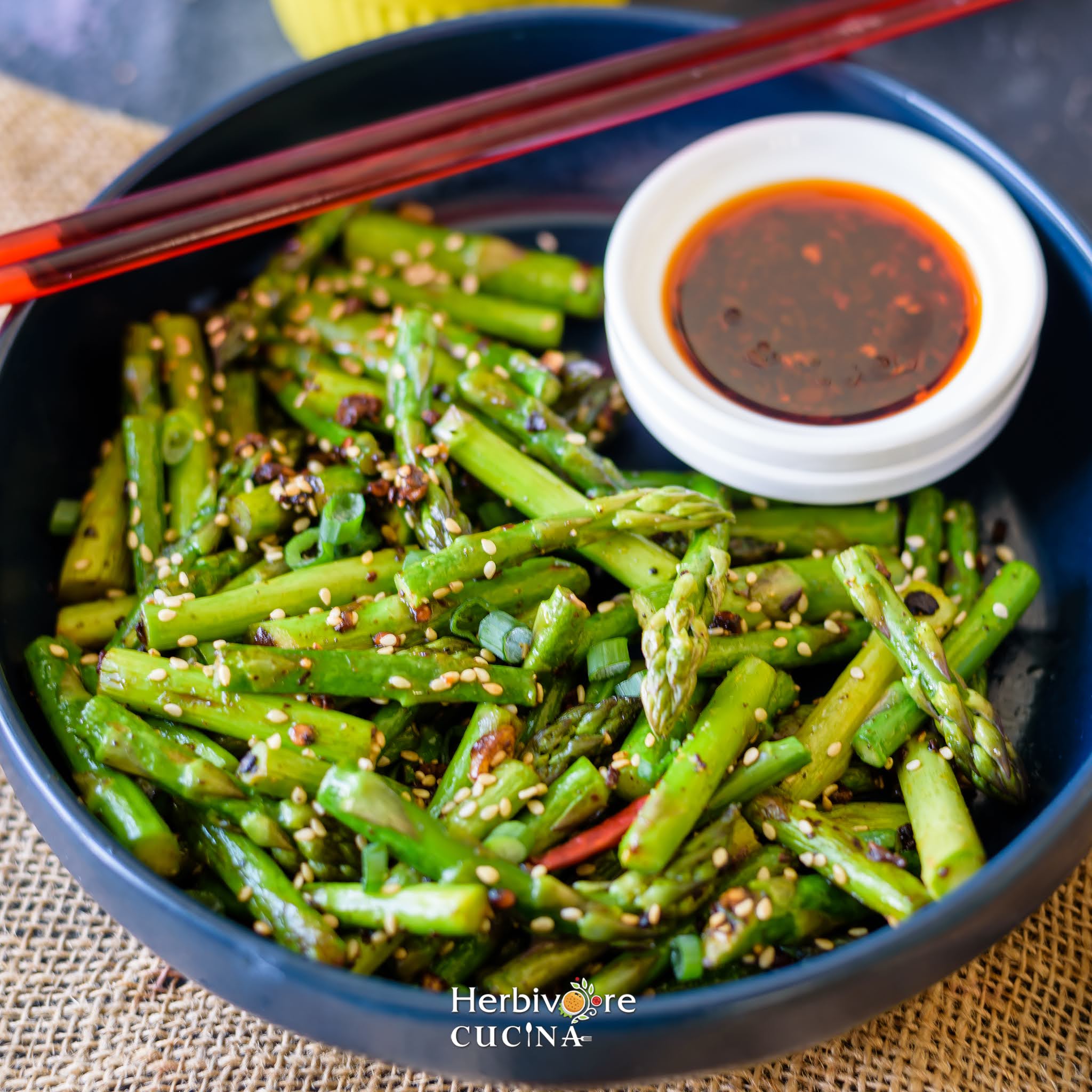 Stir Fried Asparagus in a blue bowl with chili oil placed in a small bowl beside it.