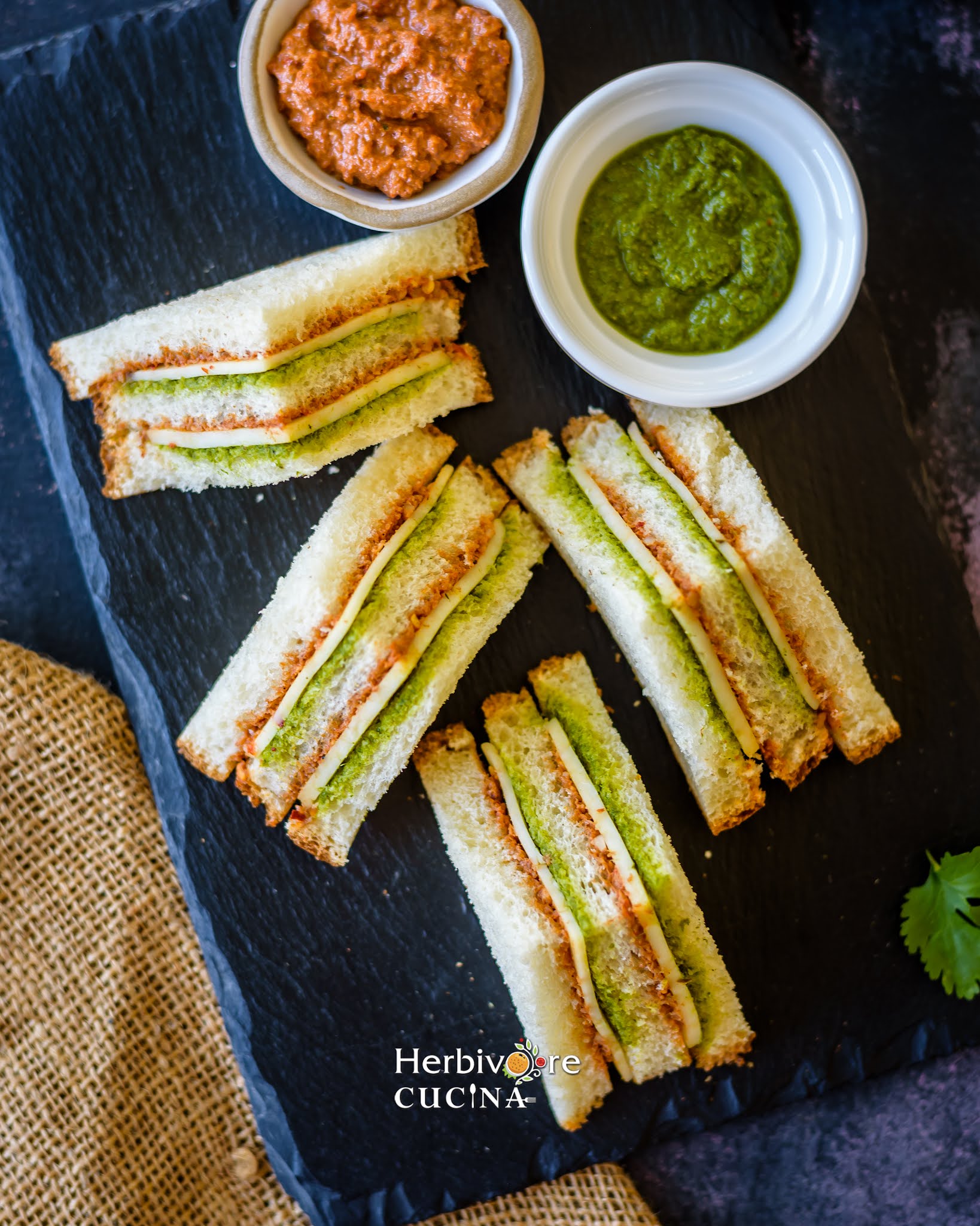 Tricolor sandwiches on a slate platter with a dip and chutney on the side. 