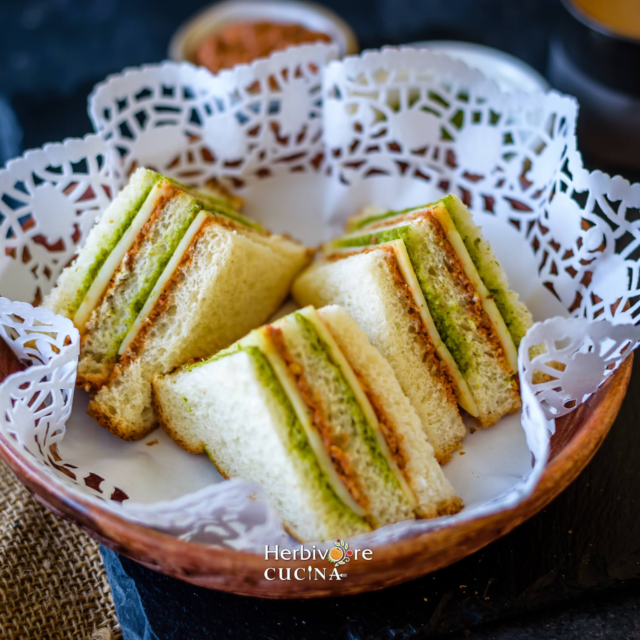 Three tricolor sandwich slices placed on a tea doily and served in a wooden plate.  