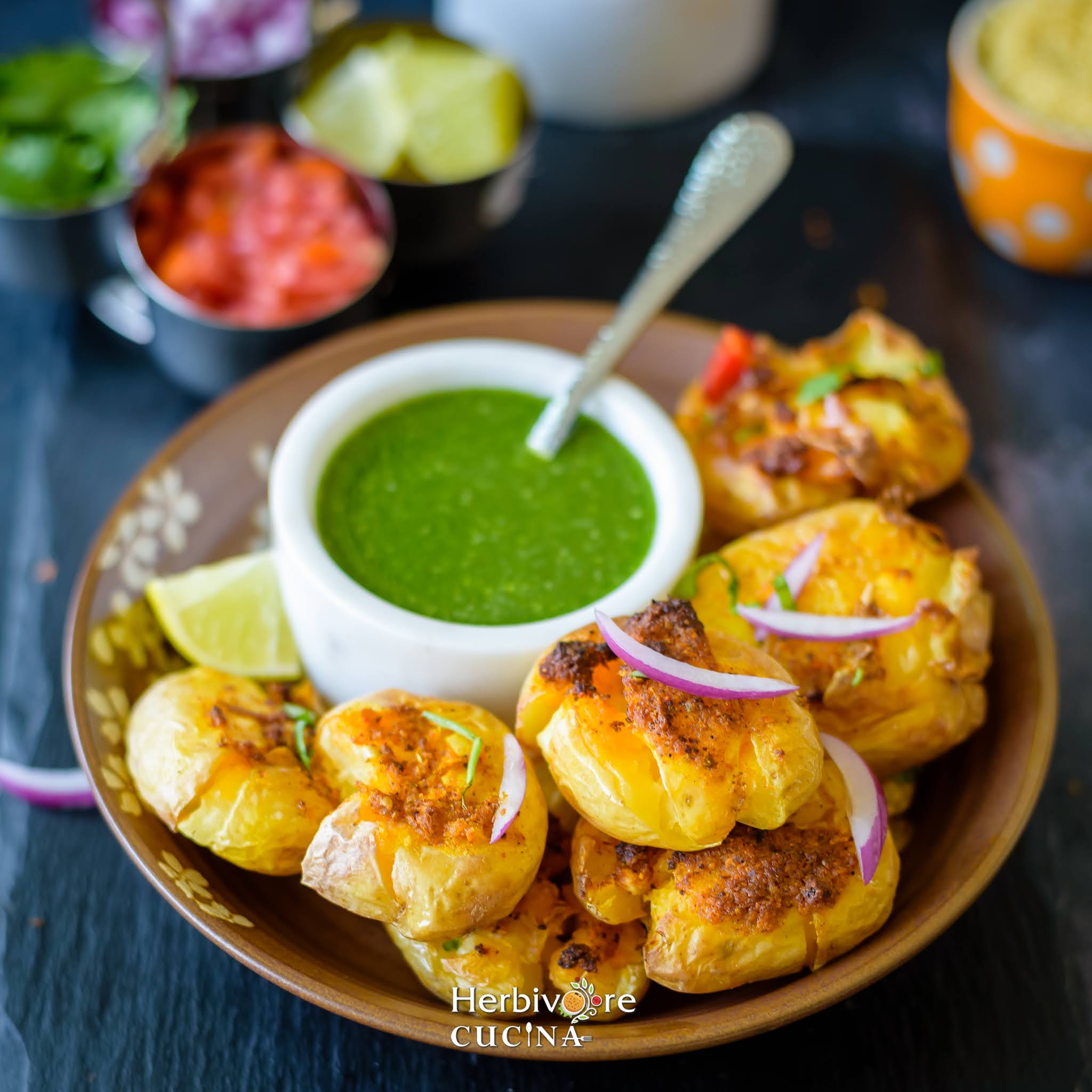 Air Fried Masala Smashed Potatoes in a plate with cilantro chutney and topped with onions and lemons. 