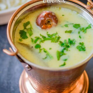 A copper mini bucket filled with Gujarati kadhi served with rice and papad on the side.