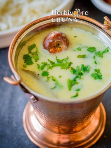 A copper mini bucket filled with Gujarati kadhi served with rice and papad on the side.