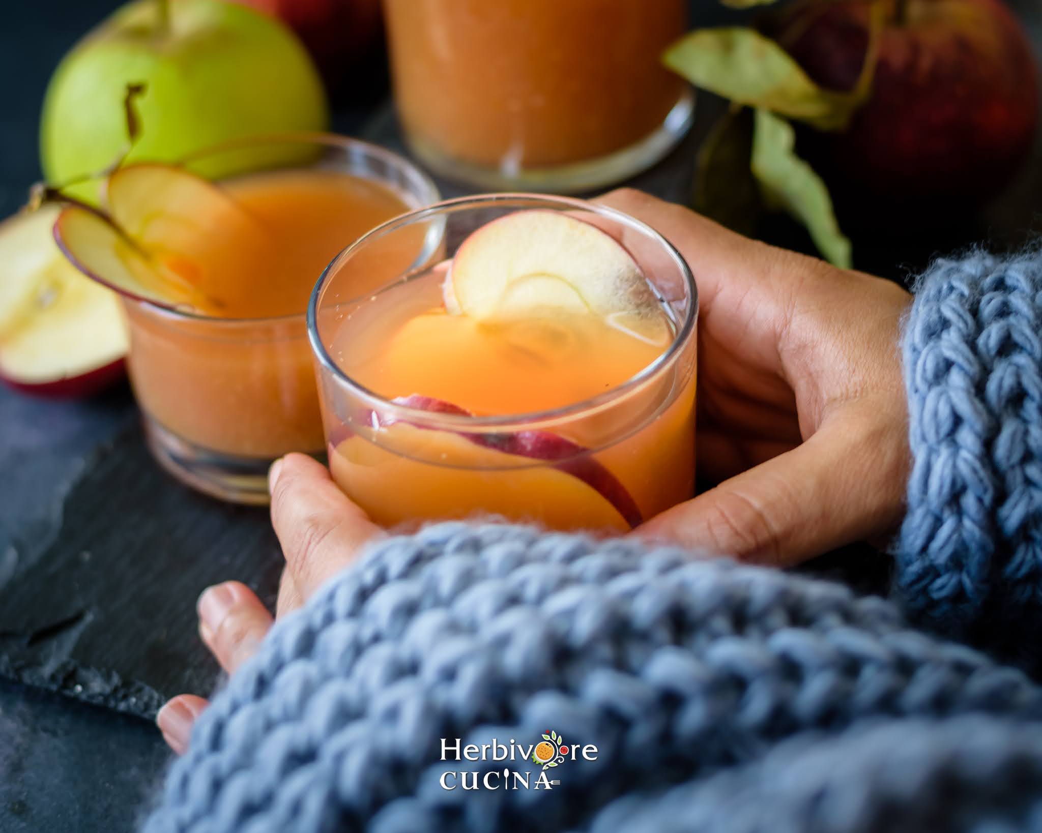 Instant Pot Apple Cider in a glass with a slice of apple held with a scarf on the hands. 