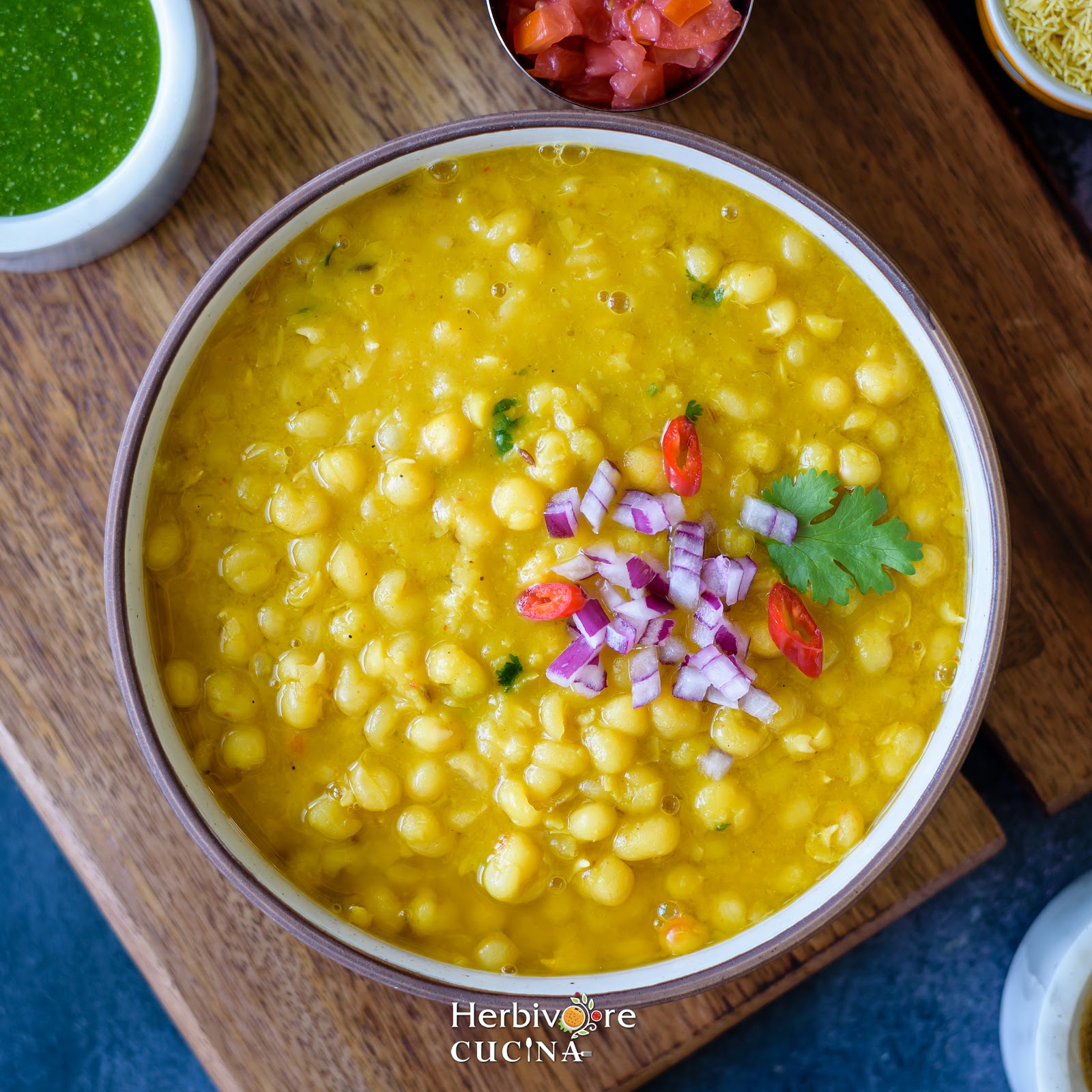 Yellow peas cooked in the instant pot served in a black bowl with chutney and chopped vegetables on the side on a wooden board. 