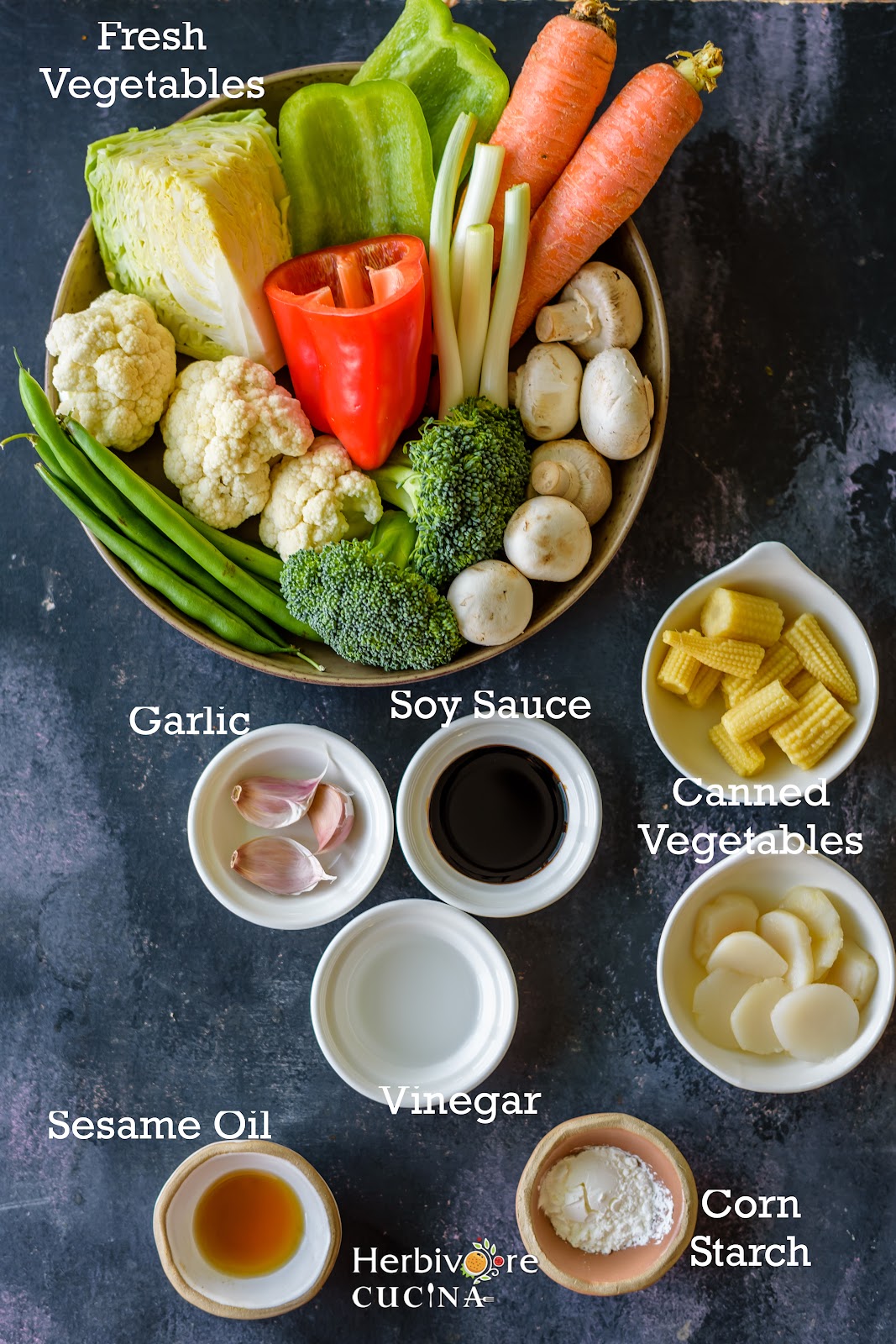 Vegetable stir fry ingredients; vegetables, sauces, seasonings and oil arranged in bowls on a black board. 