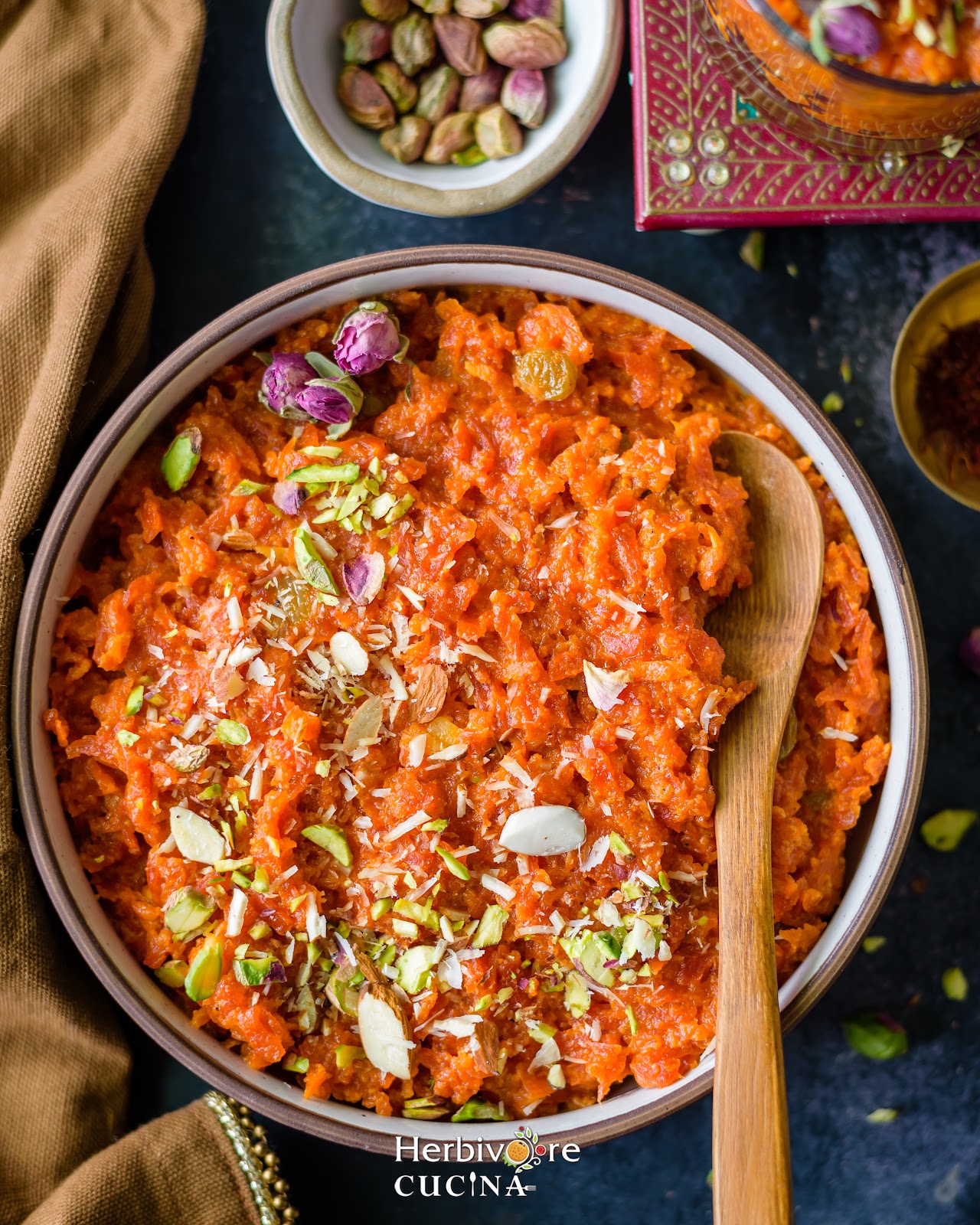 A bowl with gajar halwa topped with nuts and roses with nuts on the side. 
