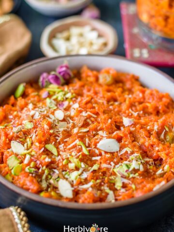 Carrot halwa in a bowl topped with shredded nuts and rose petals with nuts on the side.