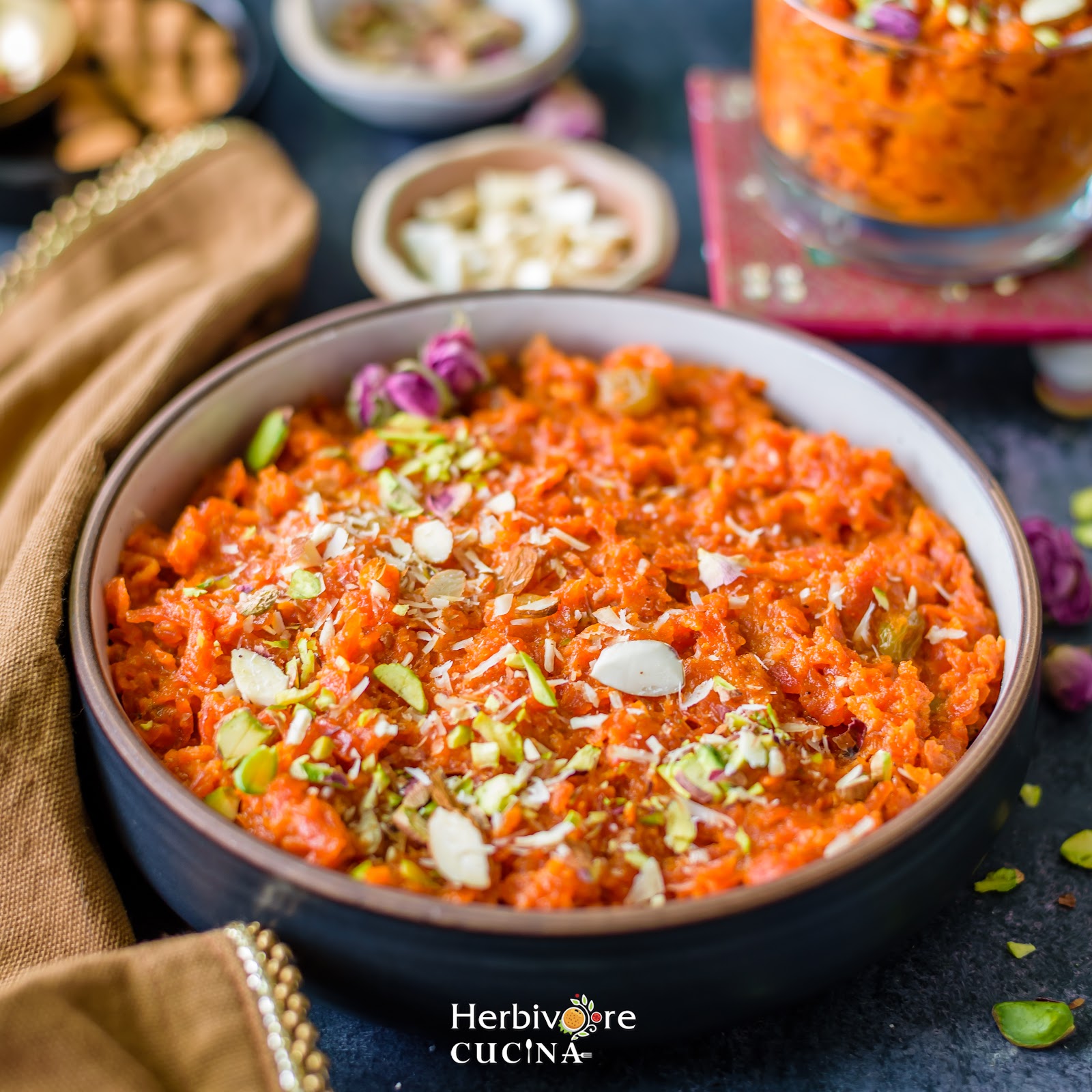 Carrot halwa in a bowl topped with shredded nuts and rose petals with nuts on the side.