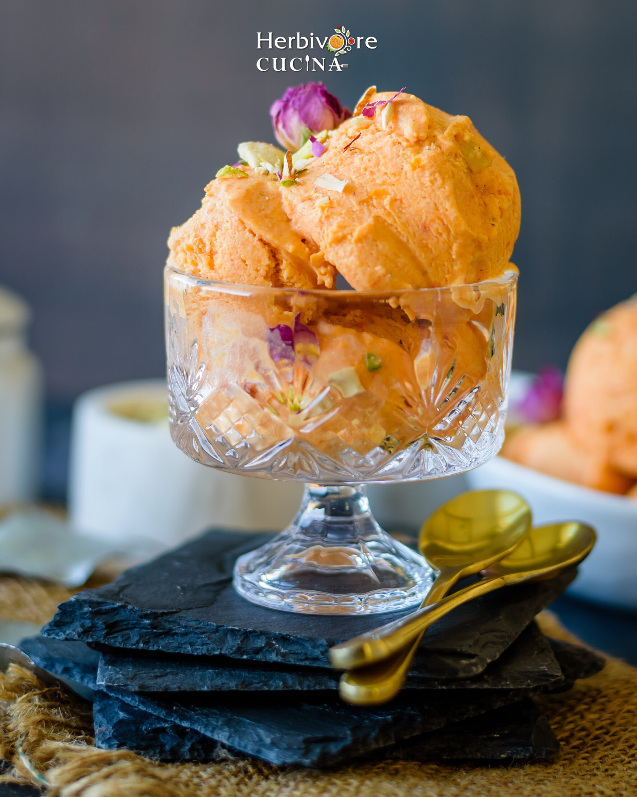 Front view of 3 scoops of gajar halwa ice cream in a clear bowl on a black slate plate on a dark background. 