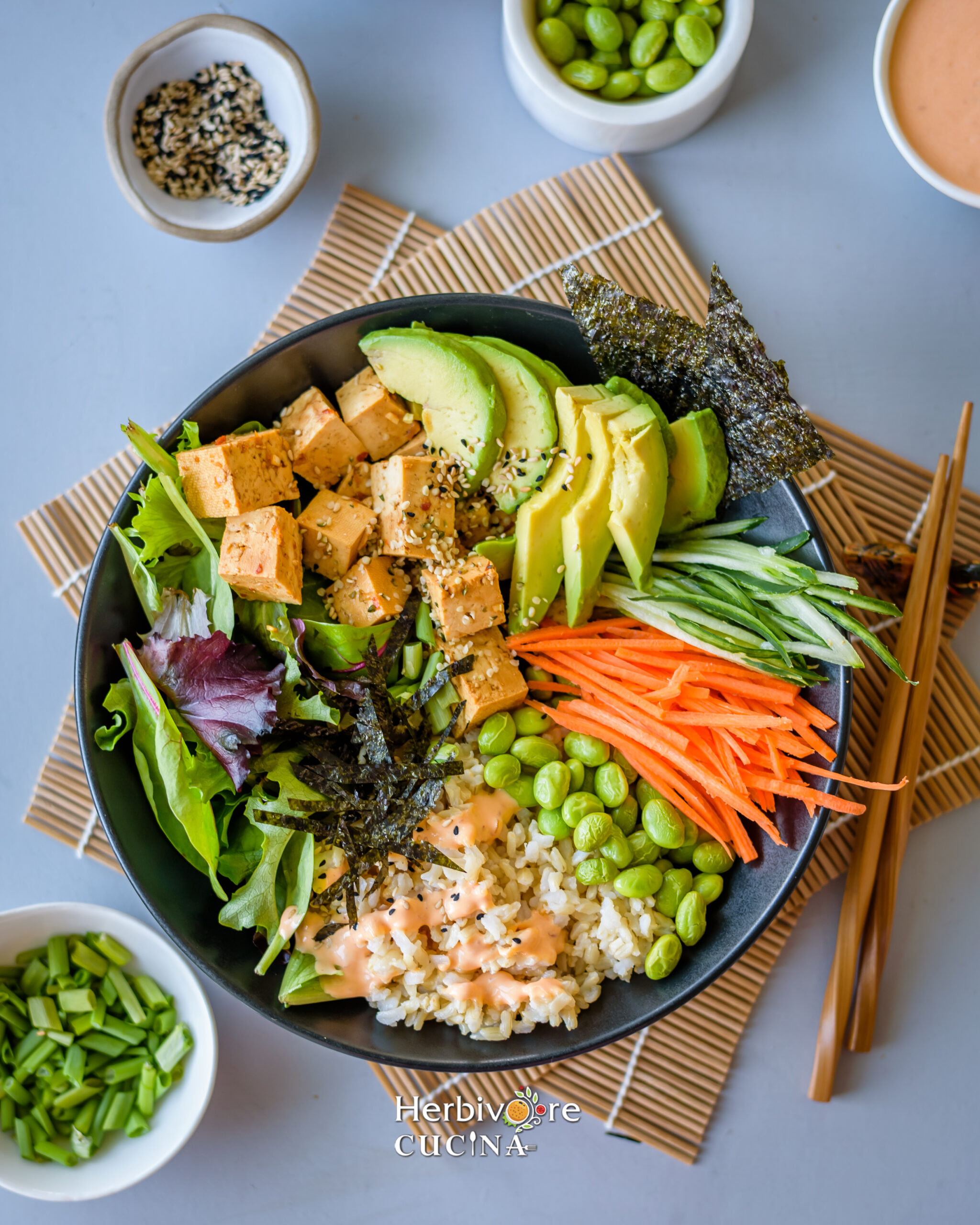 Top view of a Vegan Poke Bowl; rice, edamame, salad, nori and a delicious sauce in a black bowl on a gray background. 