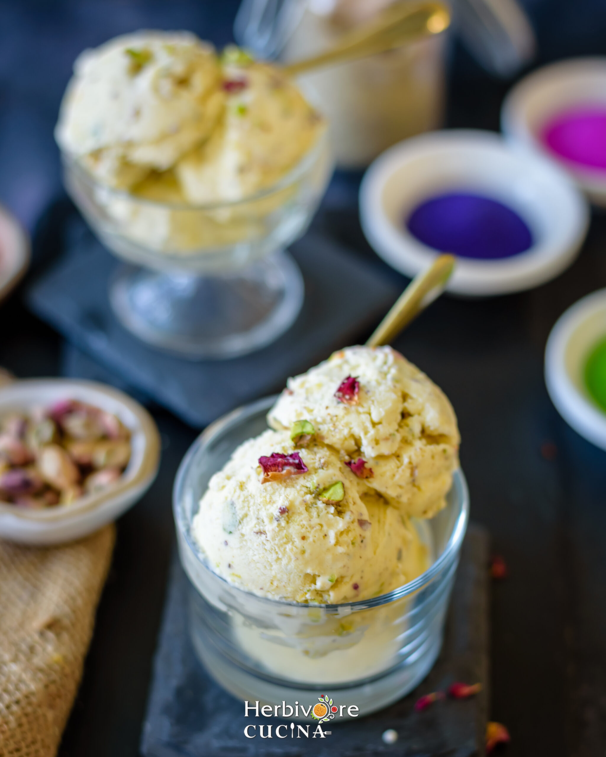 Thandai ice cream in a glass bowl with more ice cream on the side and some pistachio nuts around it on a slate platter. 