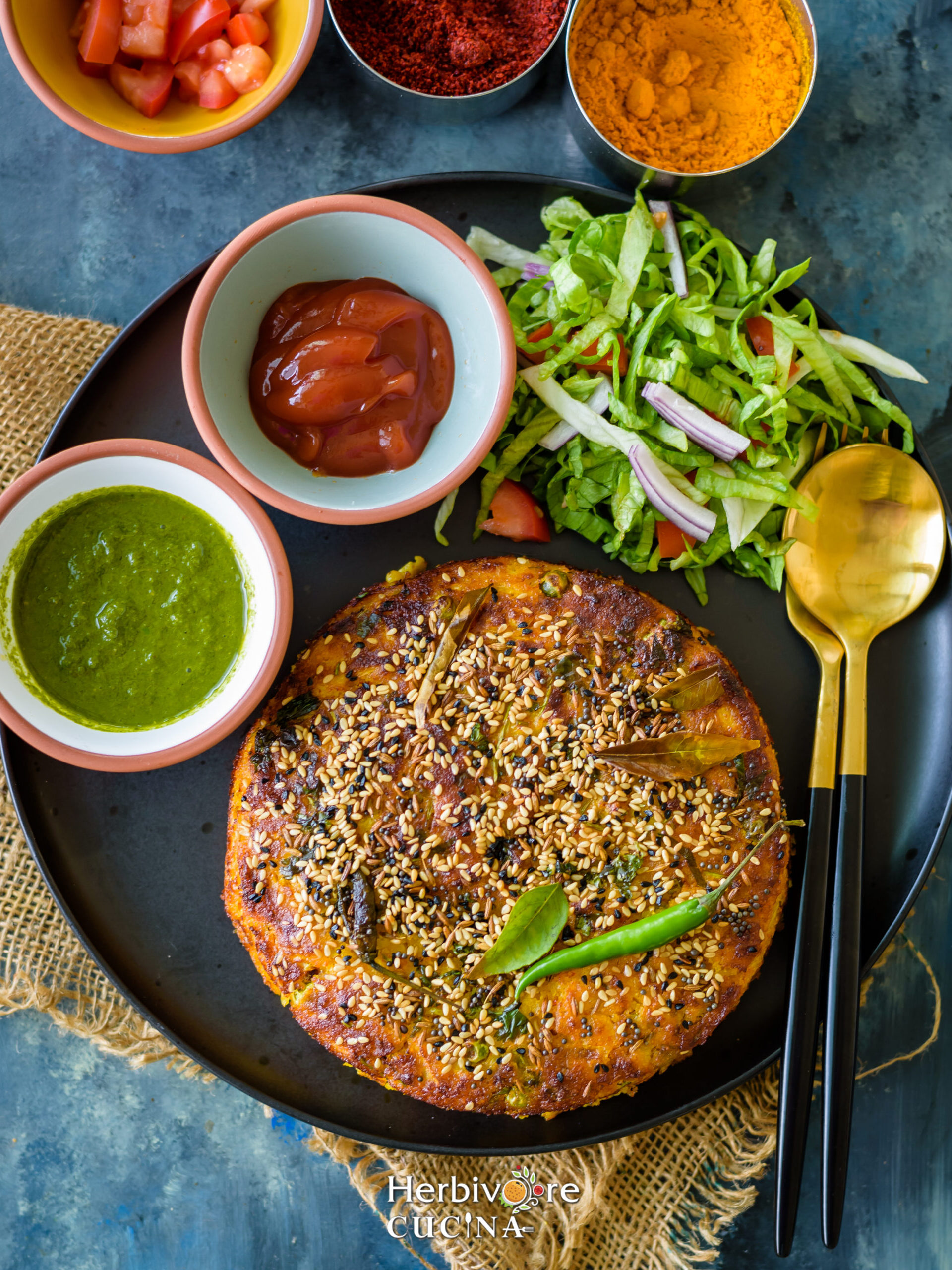 Air Fryer Handvo in a black plate with ketchup, salad and chutney on the side. 