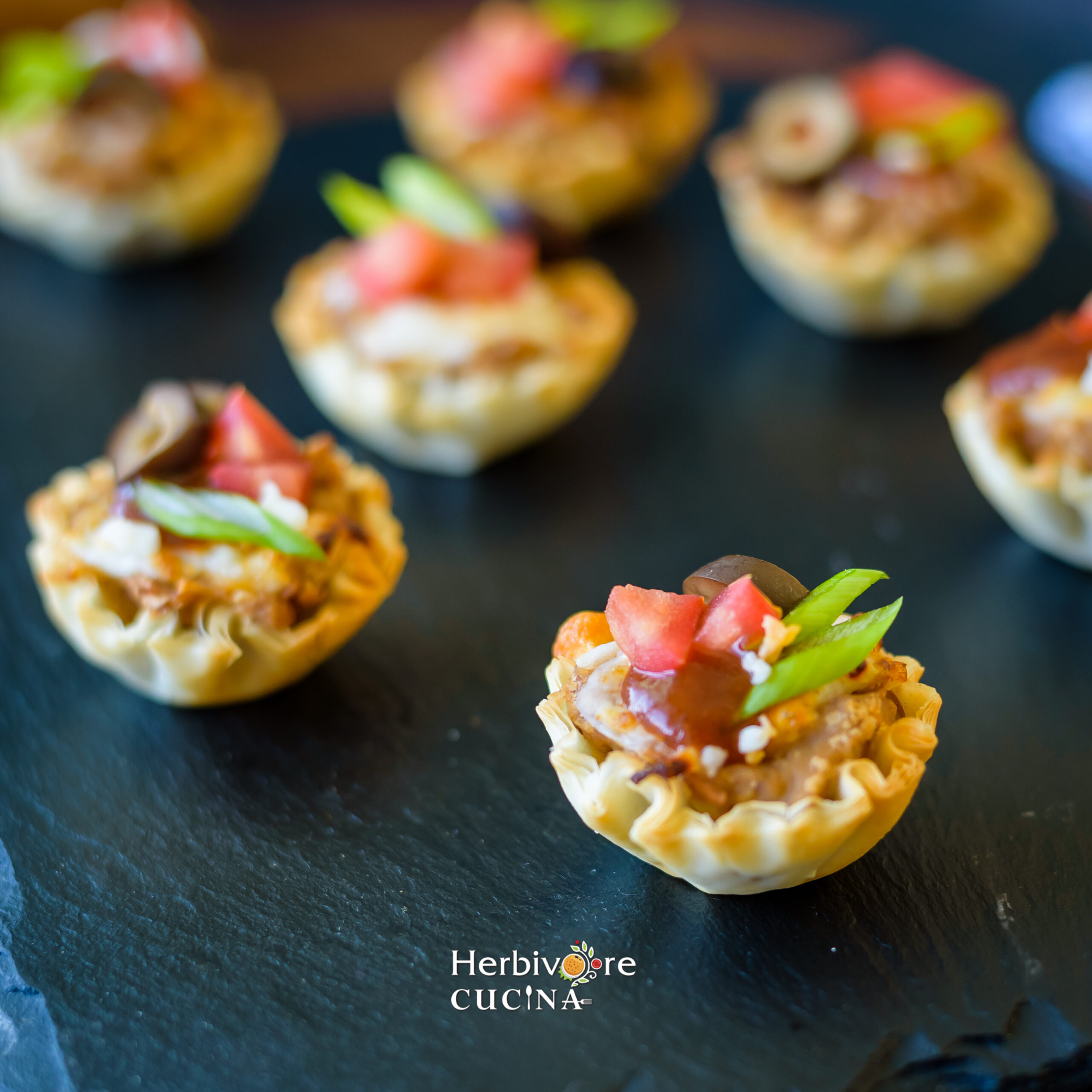 Mexican Pizza cups placed on a slate platter and topped with scallions and tomatoes. 