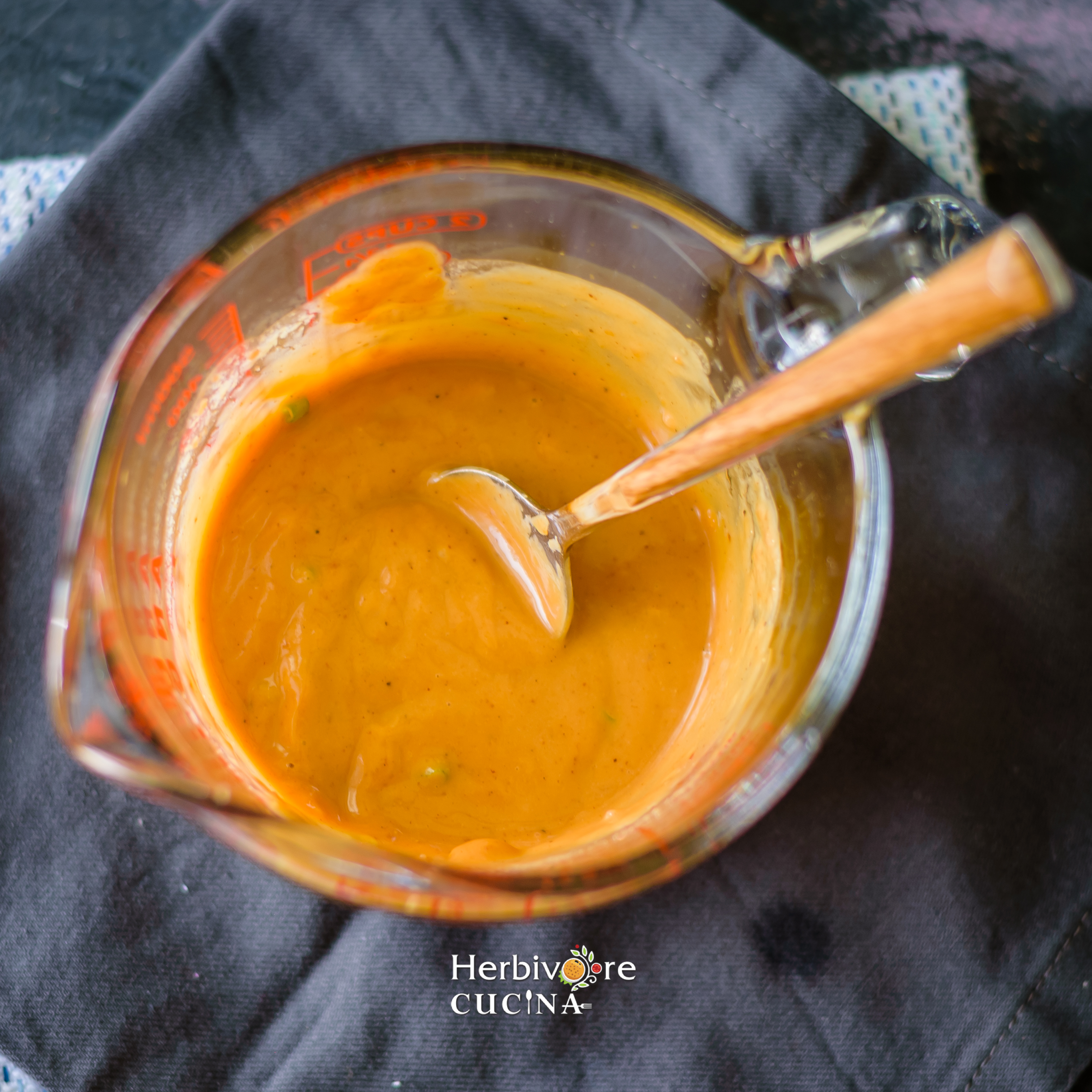 Thai Peanut sauce in a glass container with a spoon on a dark background. 