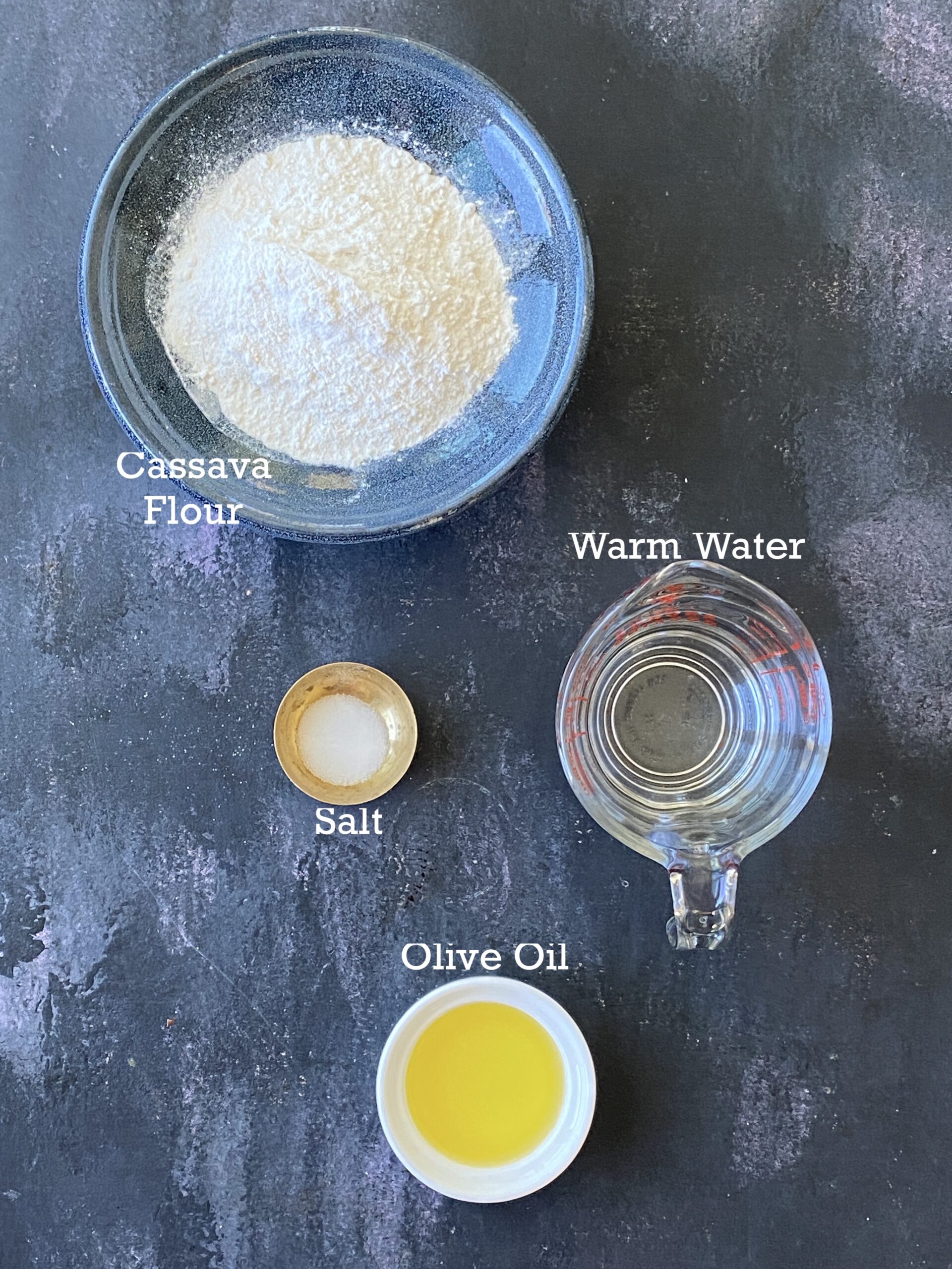 Ingredients for gluten-free tortillas in small bowls on a black surface. 