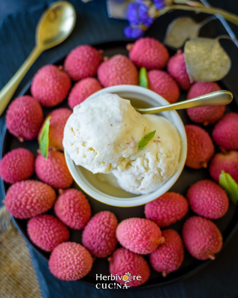 A bowl of freshly made litchi ice cream in a bowl with a spoon on the side with litchis around it. 