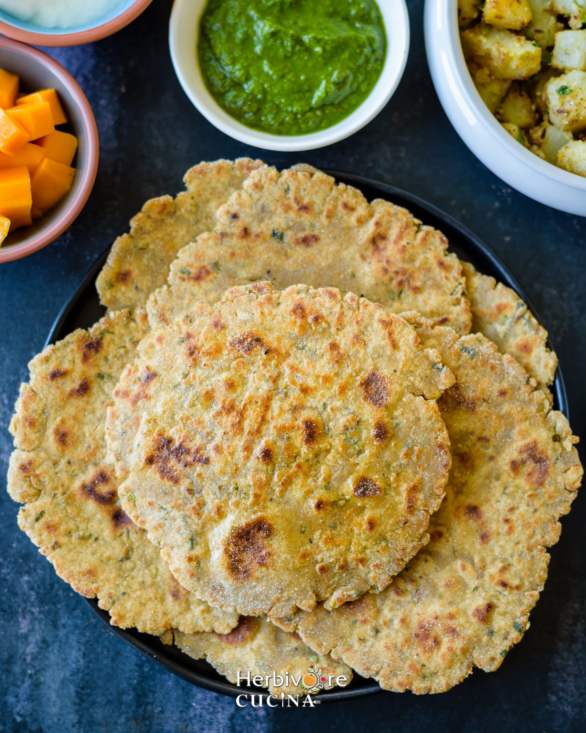 Rajgira Parathas in a black plate with cilantro chutney and sabji on the side. 