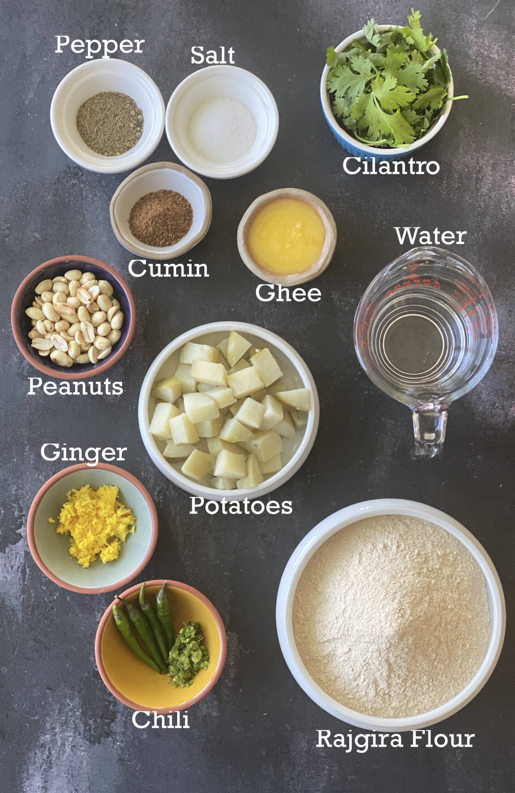 Ingredients for rajgira parathas; flour, potatoes, spices and oil all arranged in a black background. 