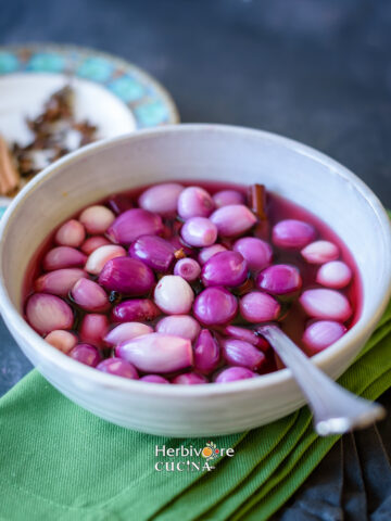 Pickled Pearl Onions in brine in a gray bowl with spices in the background on a green surface.