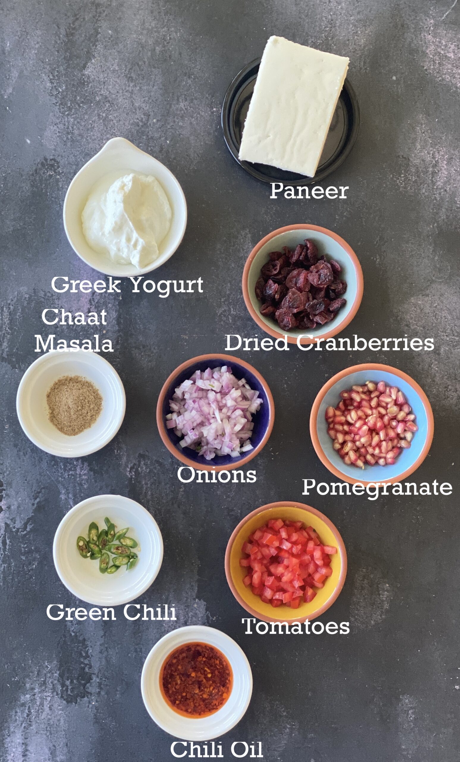 Ingredients for paneer board; paneer, Greek yogurt and add-ins and toppings arranged on a black board. 