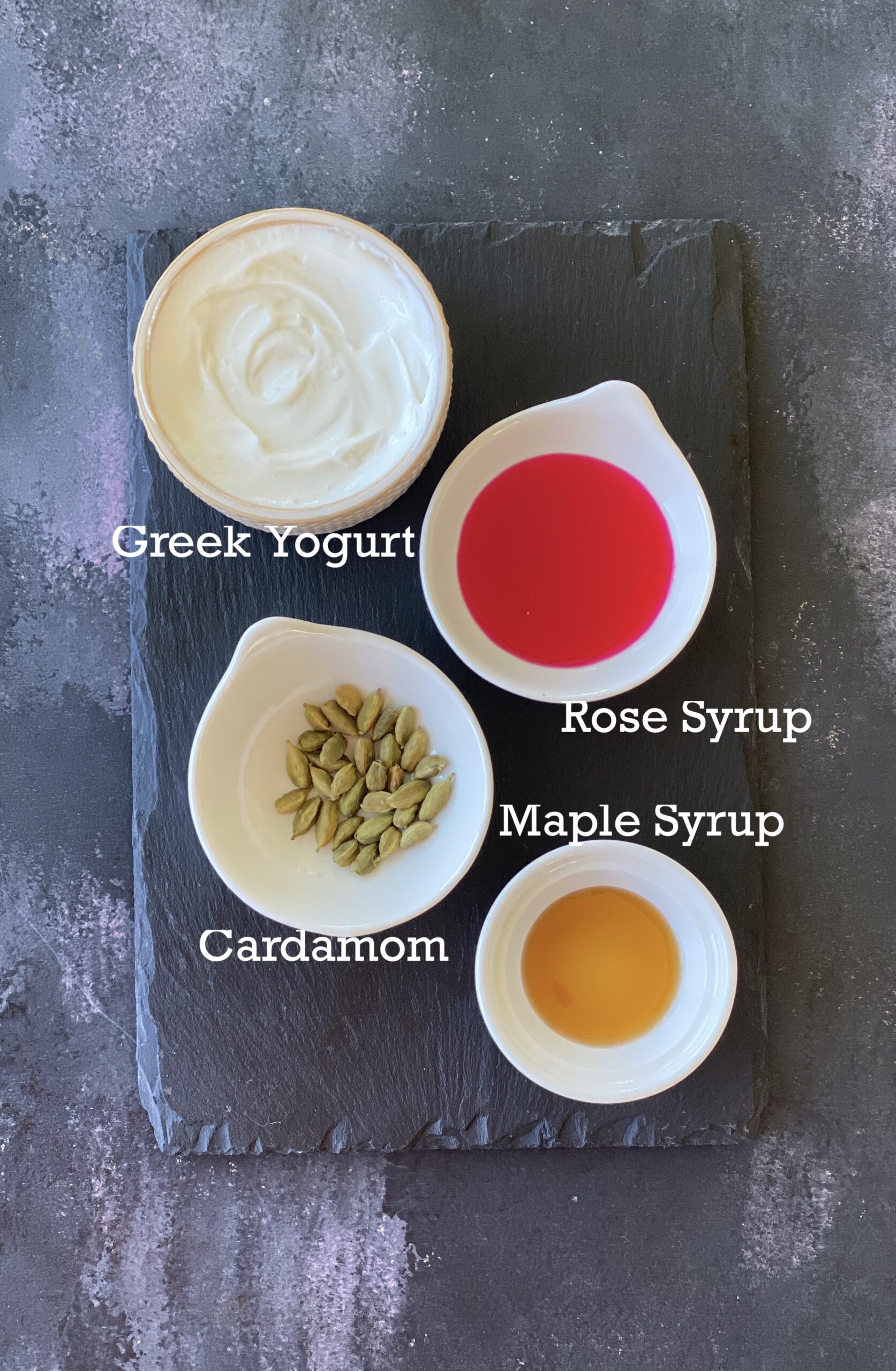 Ingredients for rose shrikhand popsicles; rose syrup, yogurt and add-ins on a slate platter. 