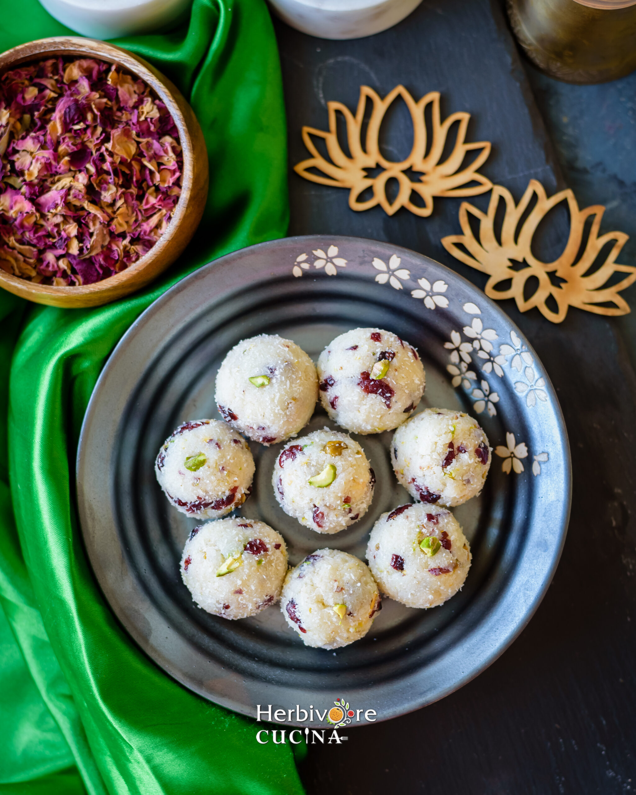 Serving cranberry pistachio truffles in a gray plate with rose petals and lotus cut-outs on the side. 