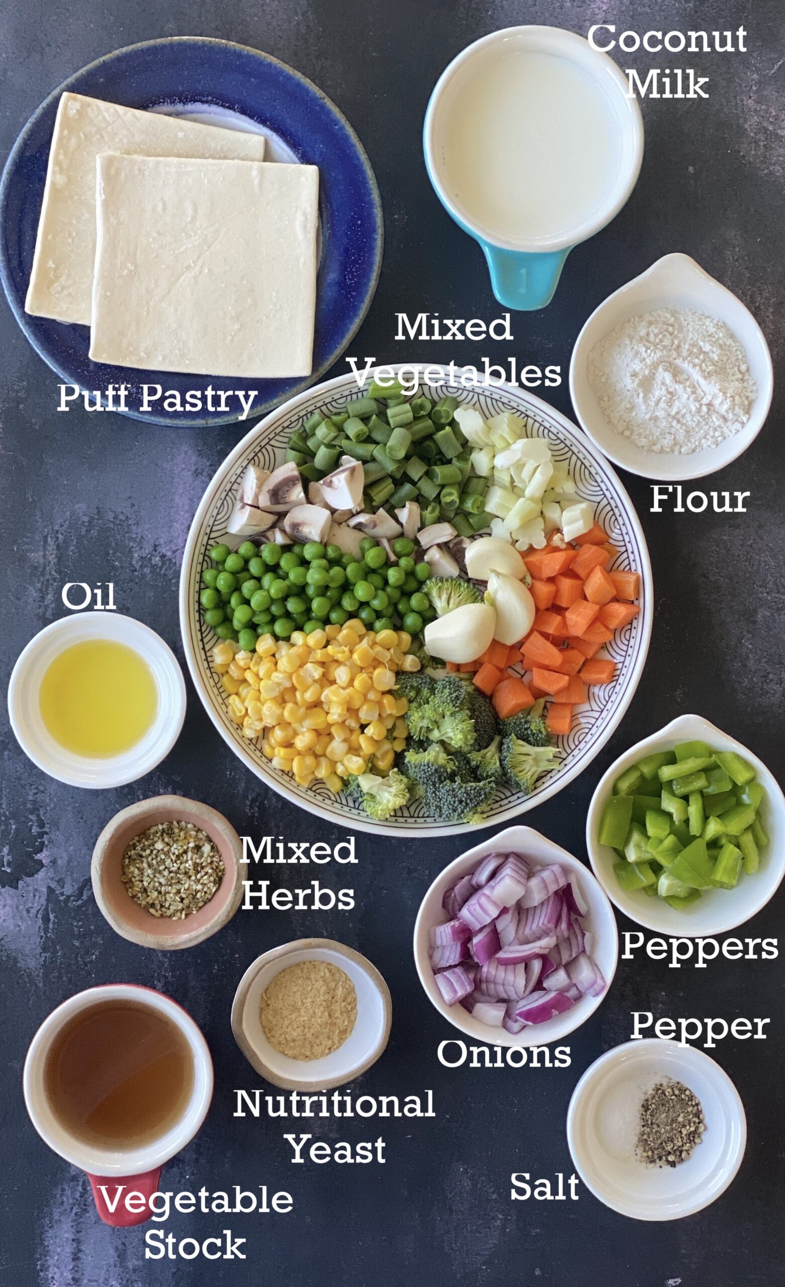 Ingredients for Air Fryer Vegetable Pot Pie; mixed vegetables, puff pastry and add-ins arranged on a dark surface. 