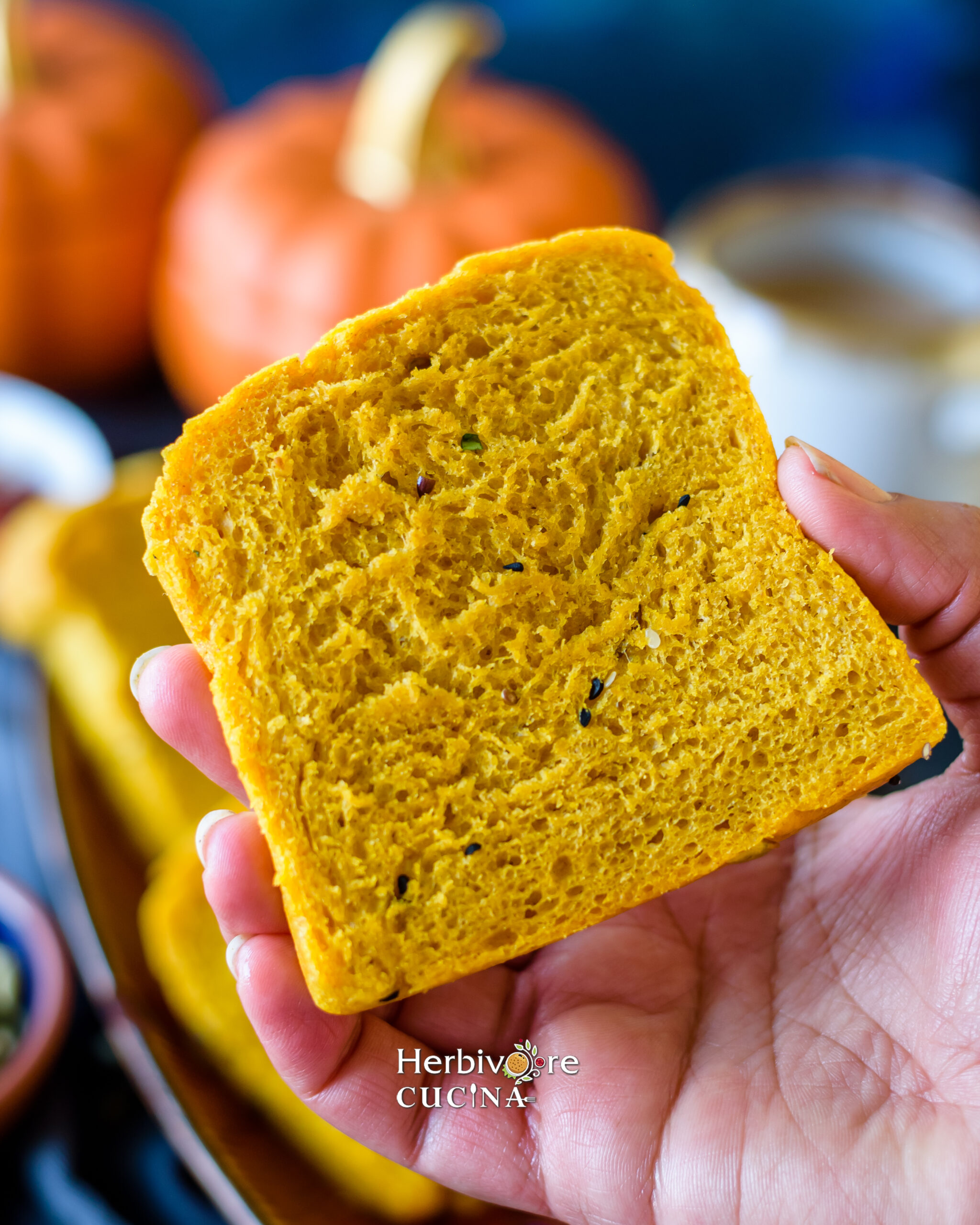 Close up of pumpkin bread in a palm with some pumpkins on the side and a cup of masala chai by it. 