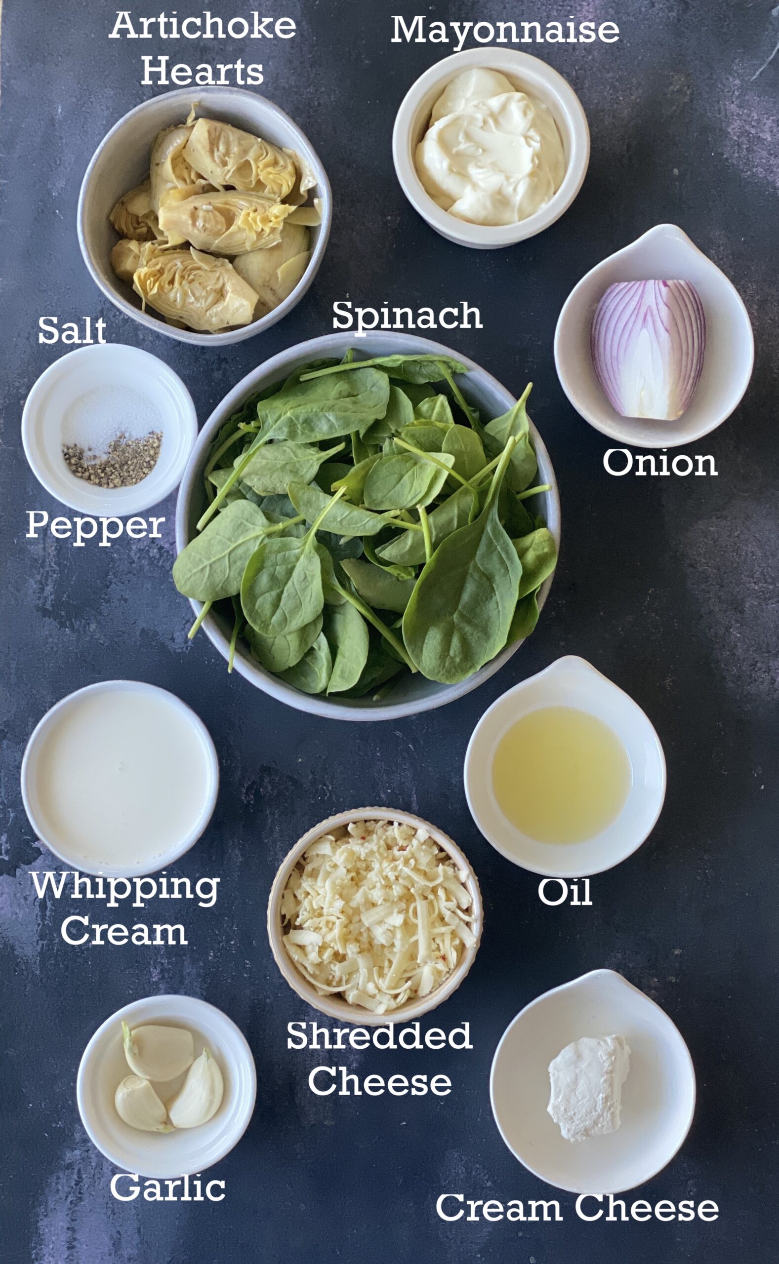 spinach artichoke dip ingredients; spinach, artichokes, cream, cheese and mayo arranged in bowls on a black surface. 