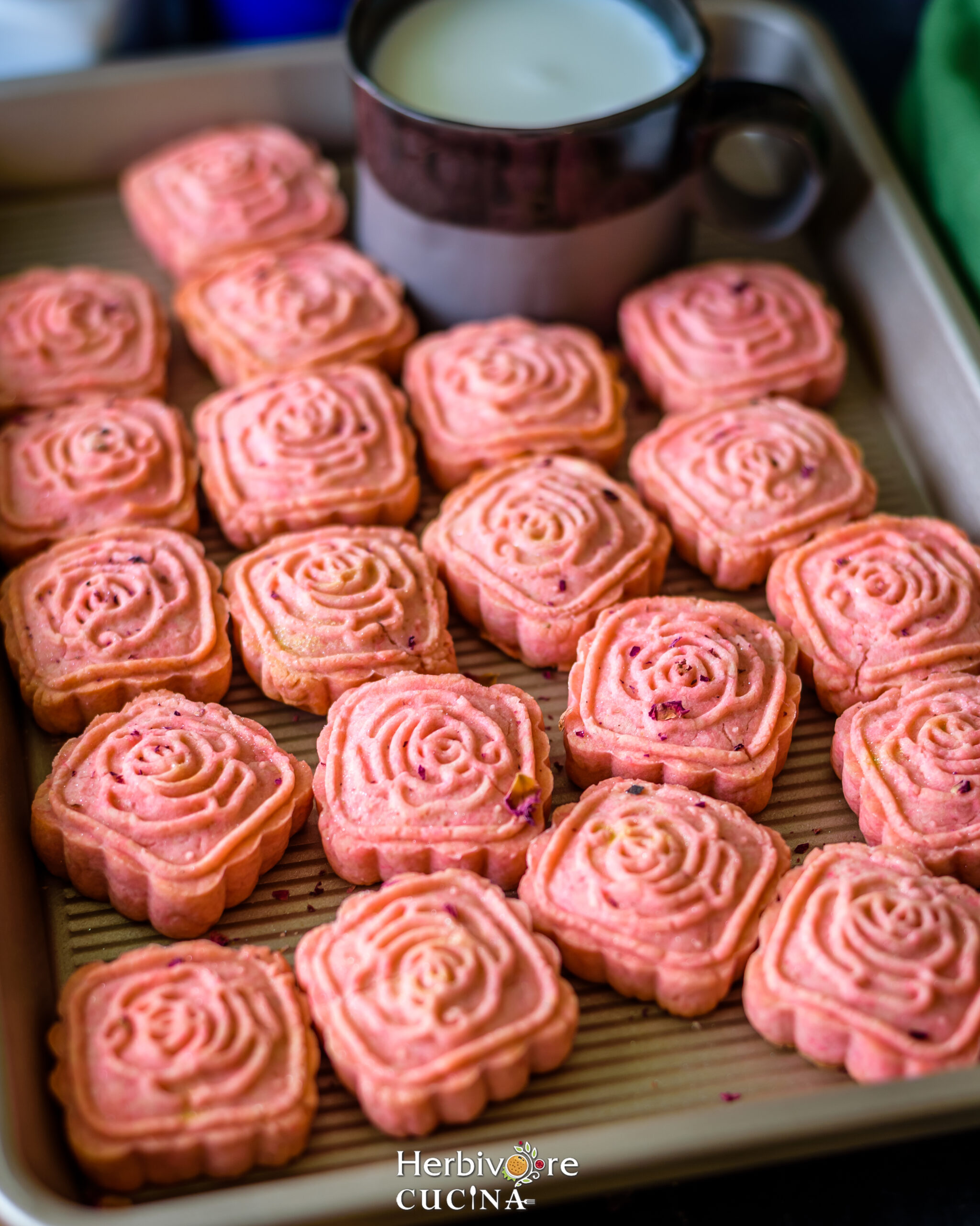 Rose cookies in a baking tray with a glass of milk on the side.  