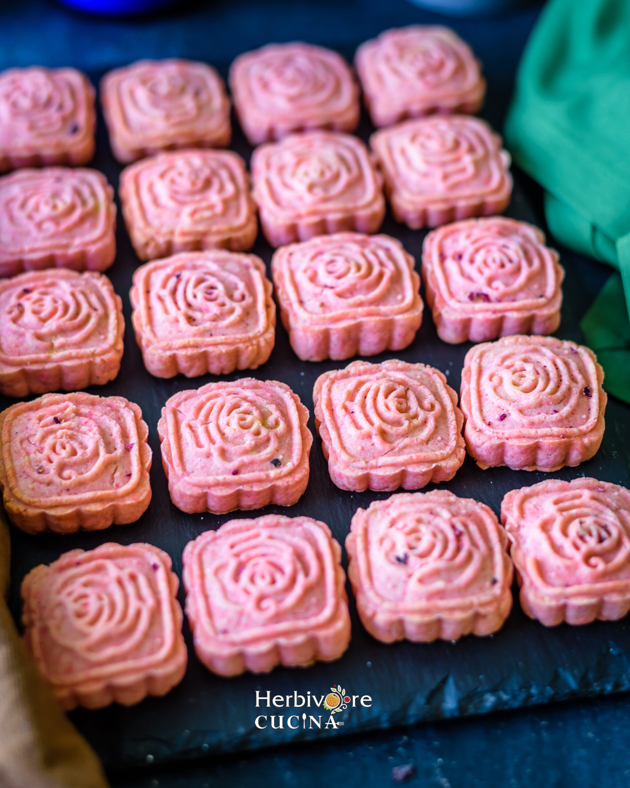 A slate platter with rose cardamom cookies and a green napkin on the side. 