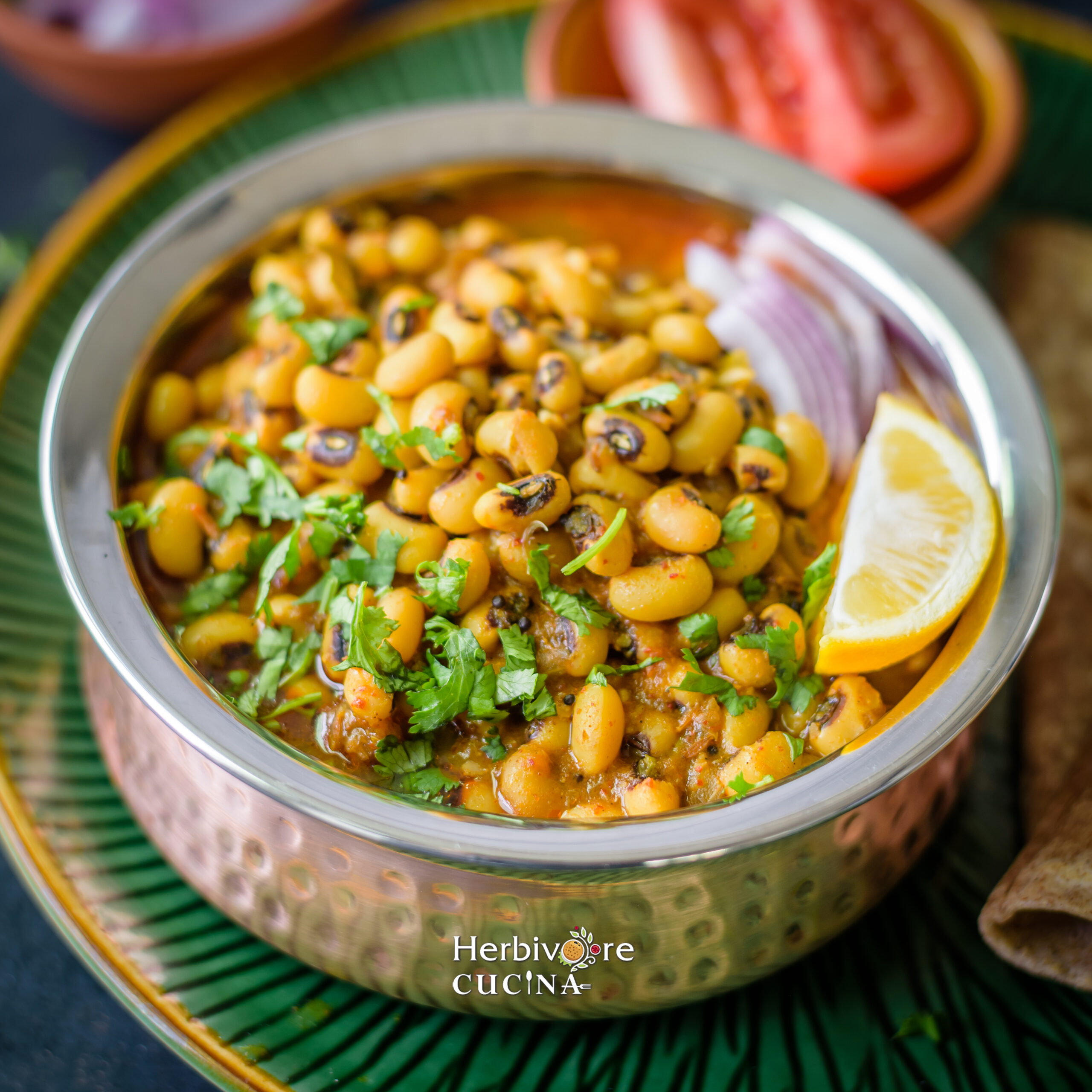 Close up of black-eyed peas curry in a copper container with some salad on it and on the side in a green plate. 