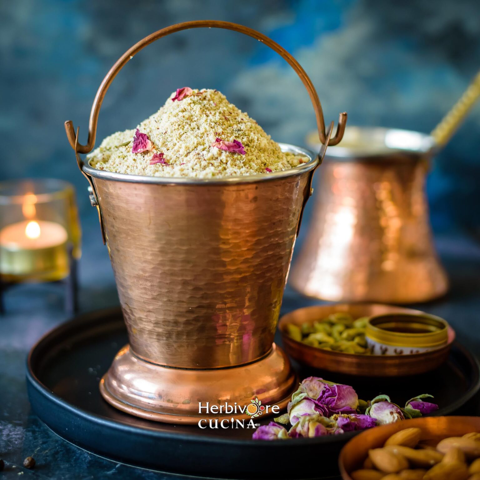 A blend of spices and nuts, Thandai Masala in a copper bucket against a dark background and rose petals on the side. 