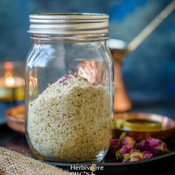 Thandai masala; a mix of spices, nuts and seeds in a glass mason jar against a dark background.