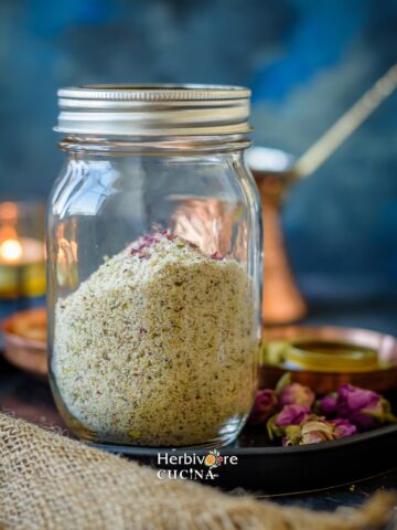 Thandai masala; a mix of spices, nuts and seeds in a glass mason jar against a dark background.