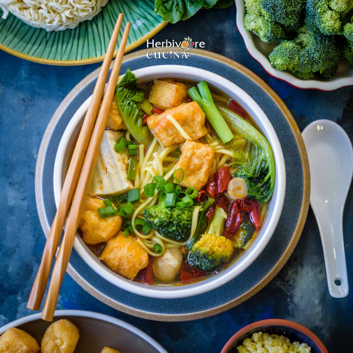 A mix of spicy Hot Pot broth with broccoli, tofu, noodles in a bowl with chopsticks. 