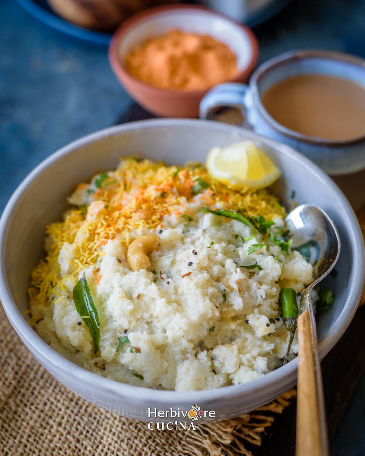 Side view of semolina upma with chutney and sev in a gray bowl with masala chai and chutney in the background.