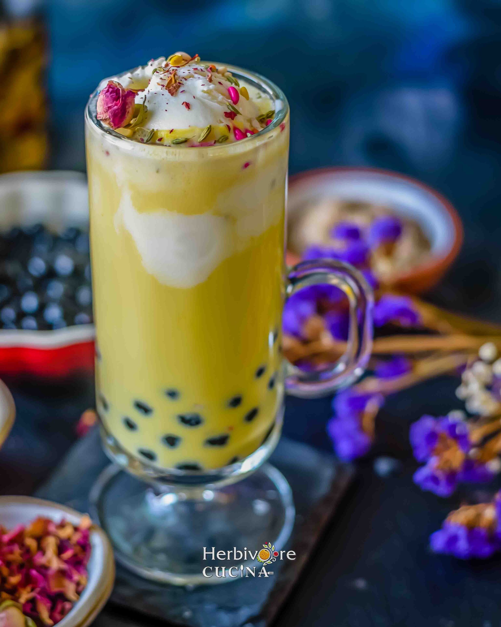 Boba thandai topped with ice-cream and all the toppings, against a backdrop with flowers and boba.