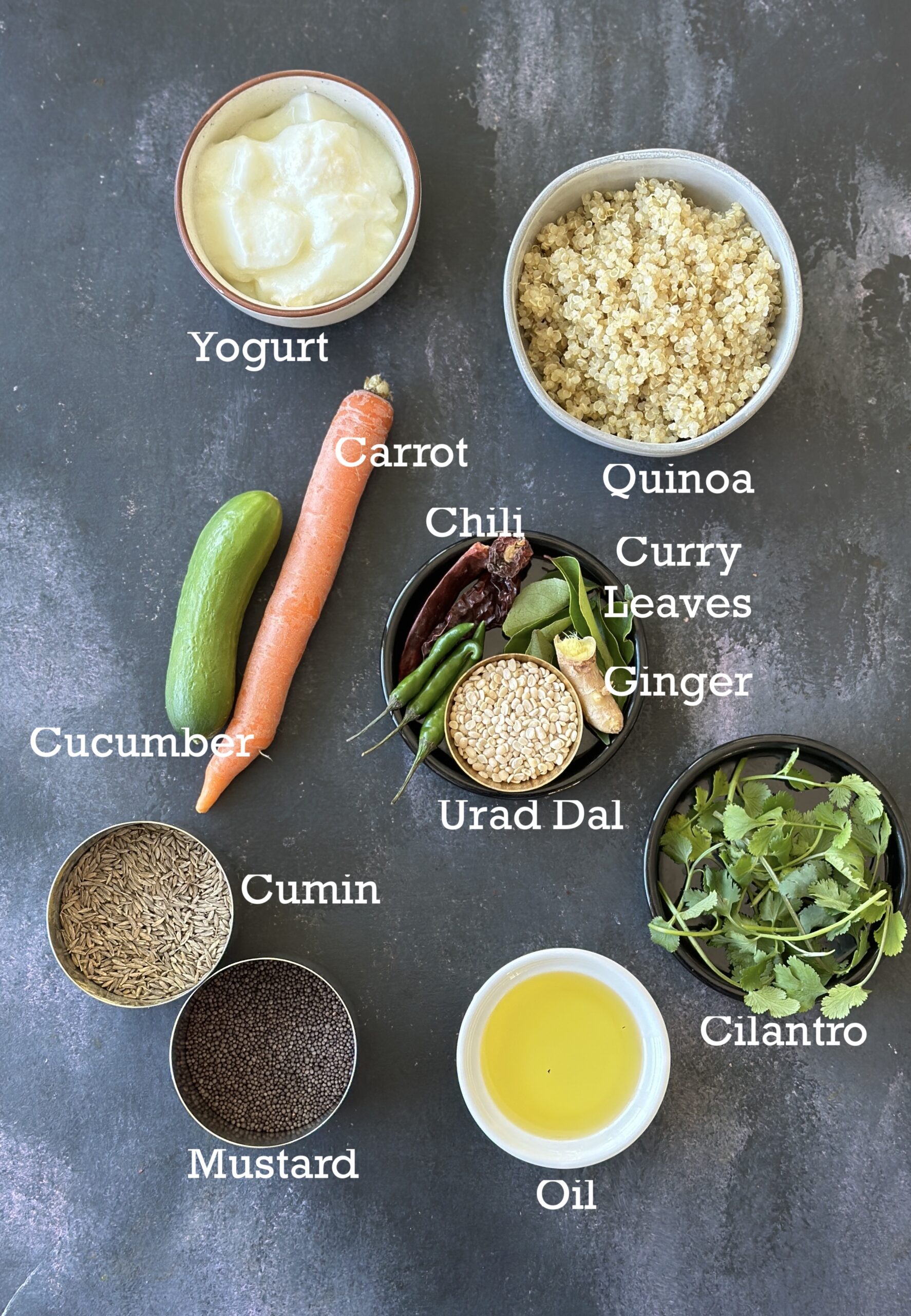Ingredients for yogurt quinoa; cooked quinoa, yogurt, vegetables and tempering spices in bowls on a black board.