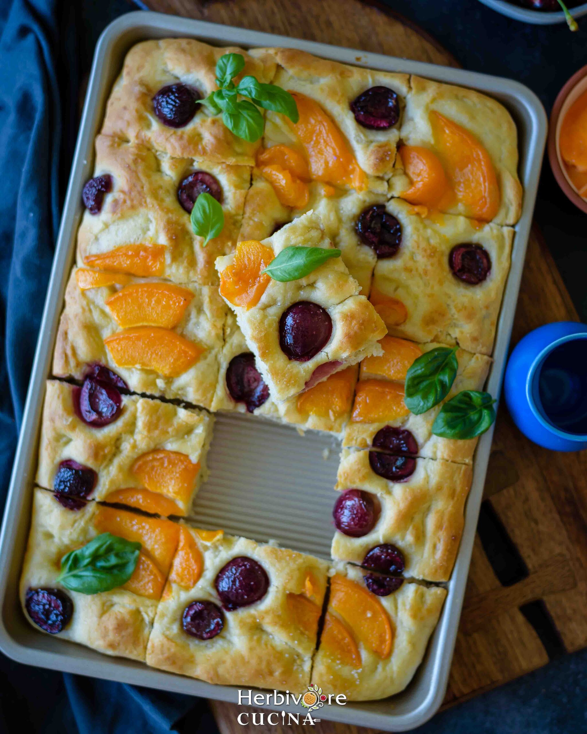 A tray with apricot and cherry focaccia with basil leaves on it arranged in a brown board. 