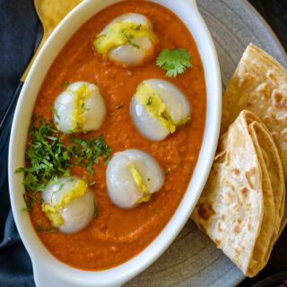 Litchi Kofta served in a white bowl with roti and salad on the side on a gray plate with a spoon and napkin around it.