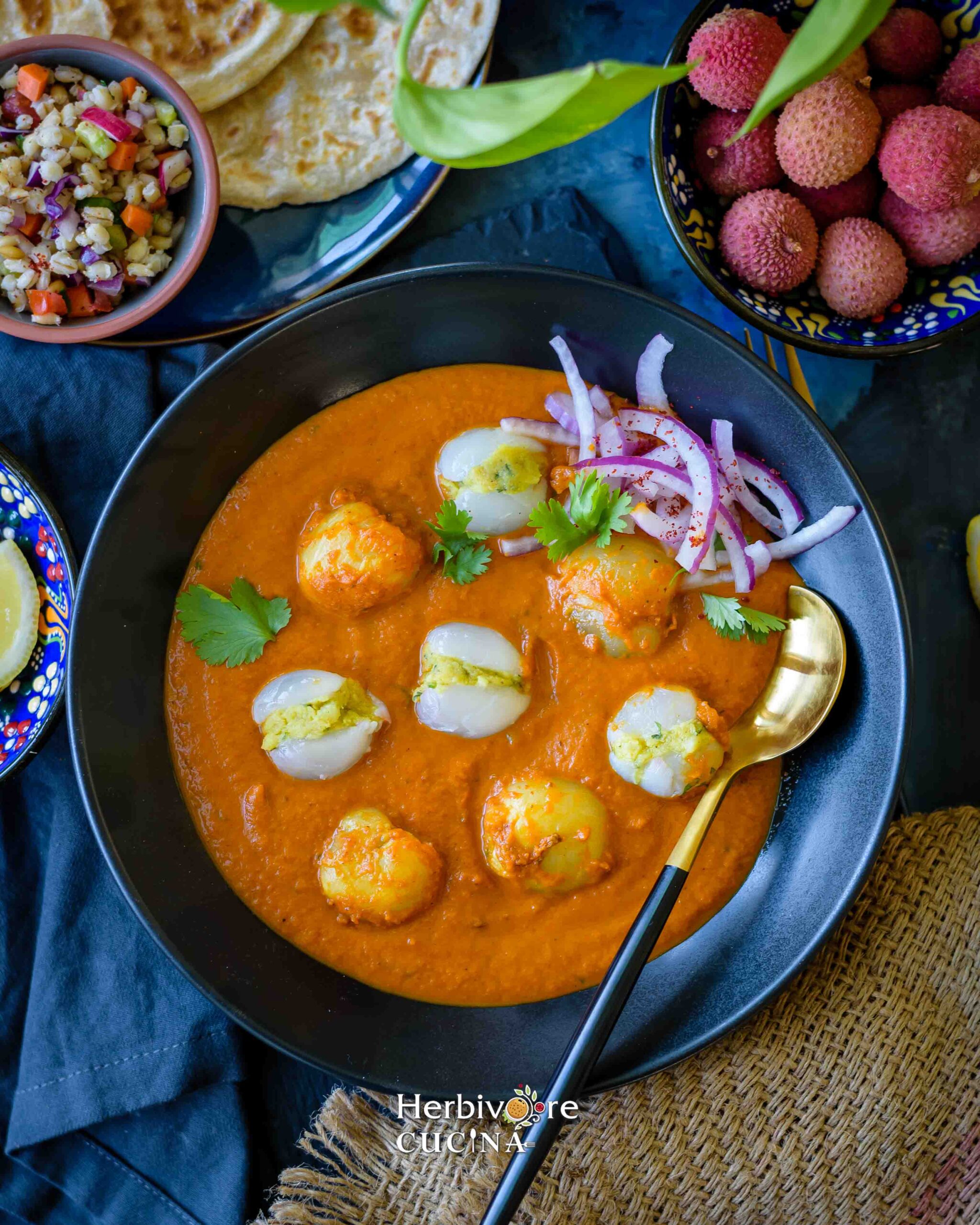 A black bowl with litchi koftas dunked in a smooth tomato gravy and served with rotis on the side. 