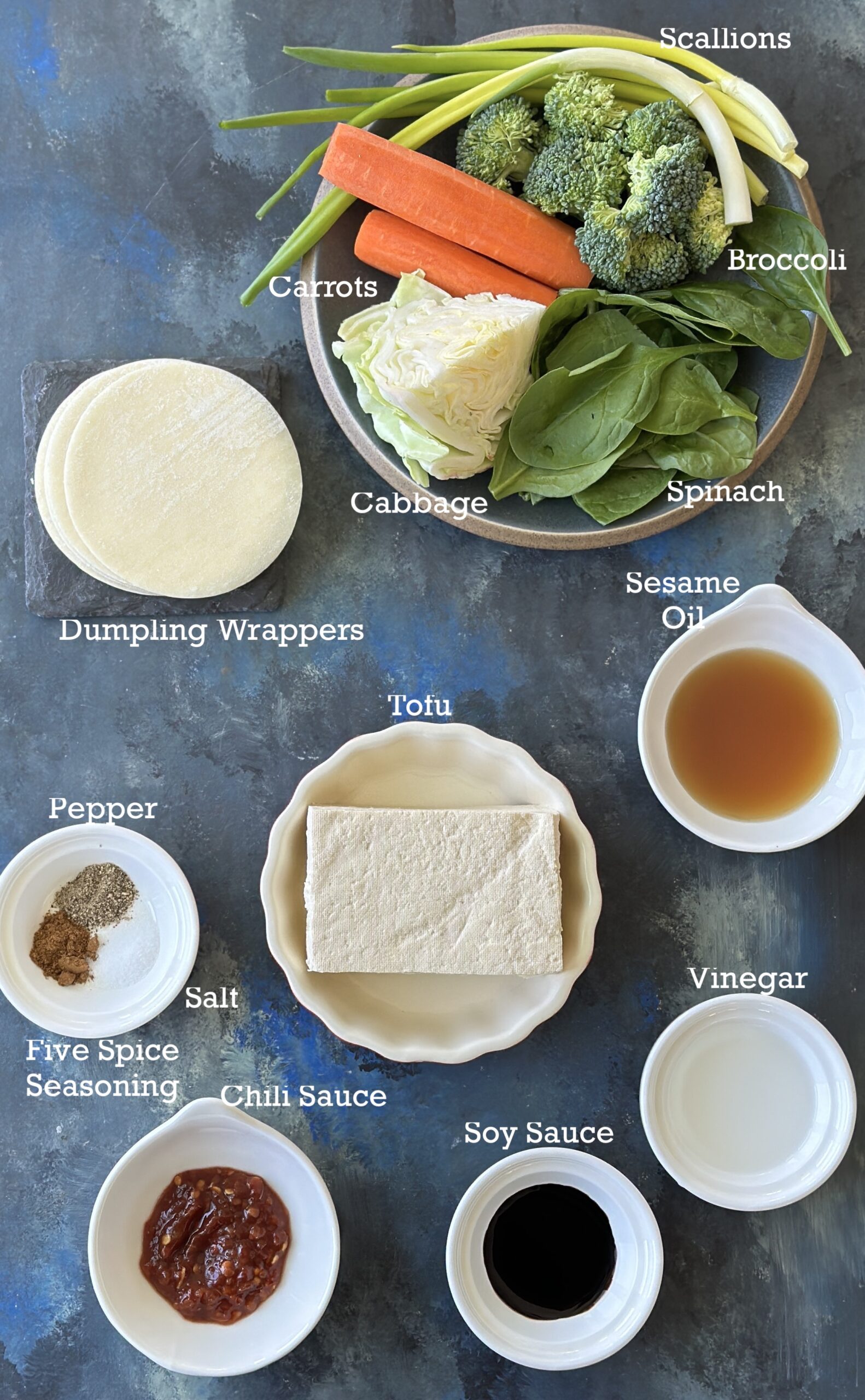 Ingredients for Pan Fried Dumplings; wrappers, vegetables, tofu and seasonings arranged on a black surface. 
