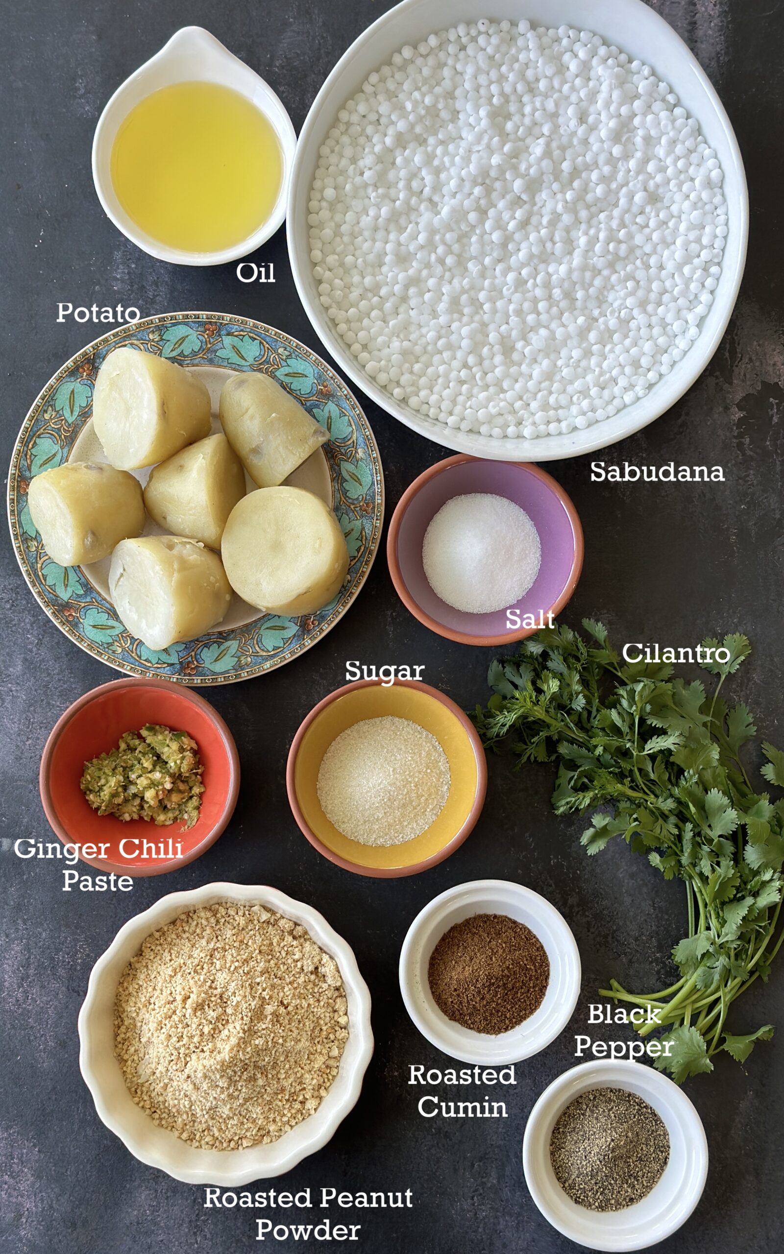 Ingredients to make Sabudana Vada; sabudana, potatoes, peanuts and spices on a black board. 