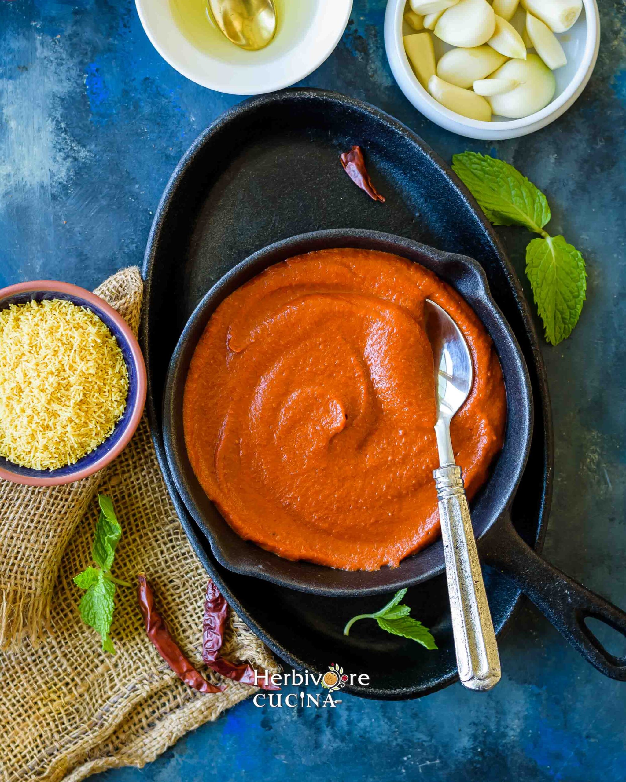 Garlic chili chutney in a black cast iron bowl with chaat ingredients around it on a blue background. 