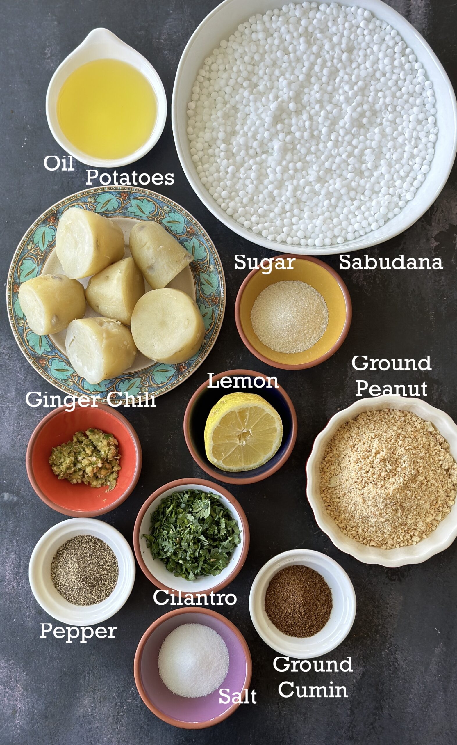 Ingredients for non-fried sabudana vada; sabudana, peanuts, potatoes and seasonings arranged on a dark background. 