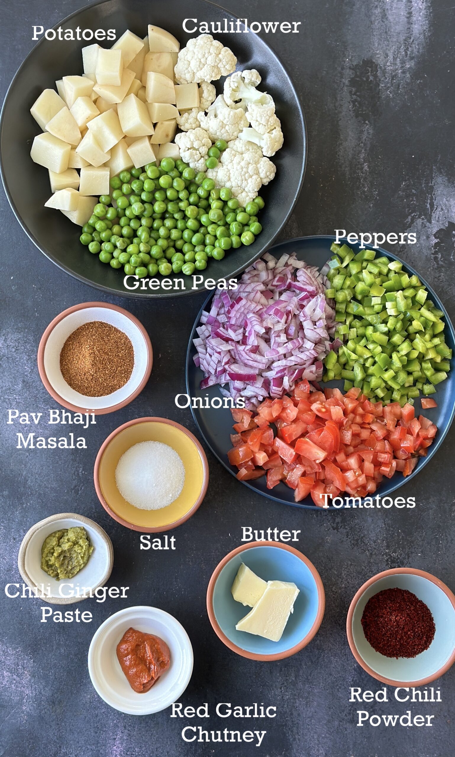 Ingredients for Pav Bhaji; vegetables, spices, butter and seasonings on a black board. 